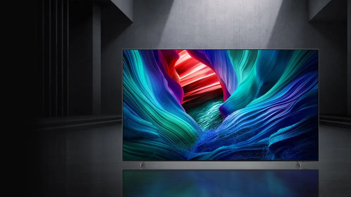 A modern flat-screen television displaying a vibrant, abstract image with swirling colors of blue, teal, purple, and red, set against a dark, minimalist background with a spotlight shining from above.