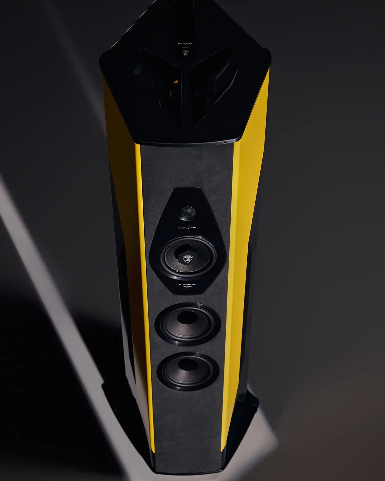 Tall, modern speaker with a black and yellow design. It features multiple drivers, including two larger woofers at the bottom, a midrange driver in the middle with the Lamborghini logo, and a smaller tweeter above it. The speaker has a sleek, angular shape with a matte finish.
