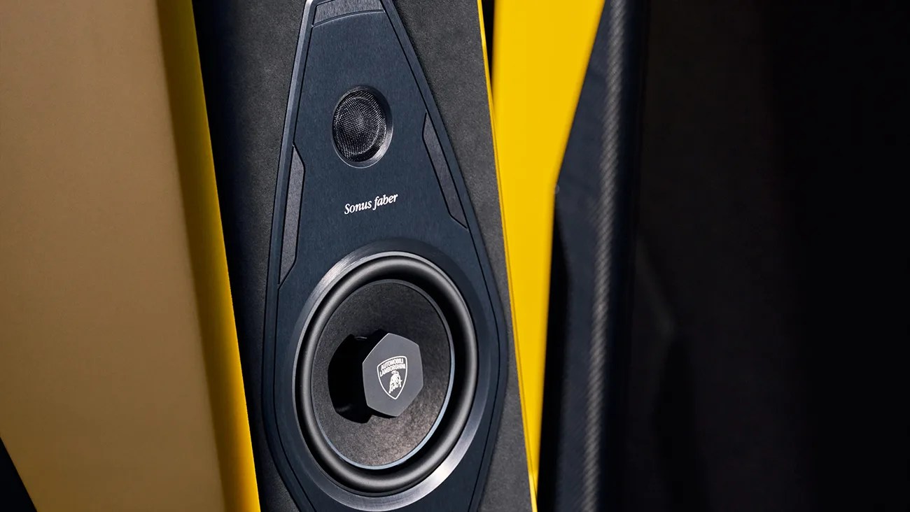 Close-up of a Sonus faber speaker integrated into a yellow and black surface, featuring a tweeter at the top and a larger woofer below with the Automobili Lamborghini logo on the woofer's center cap.