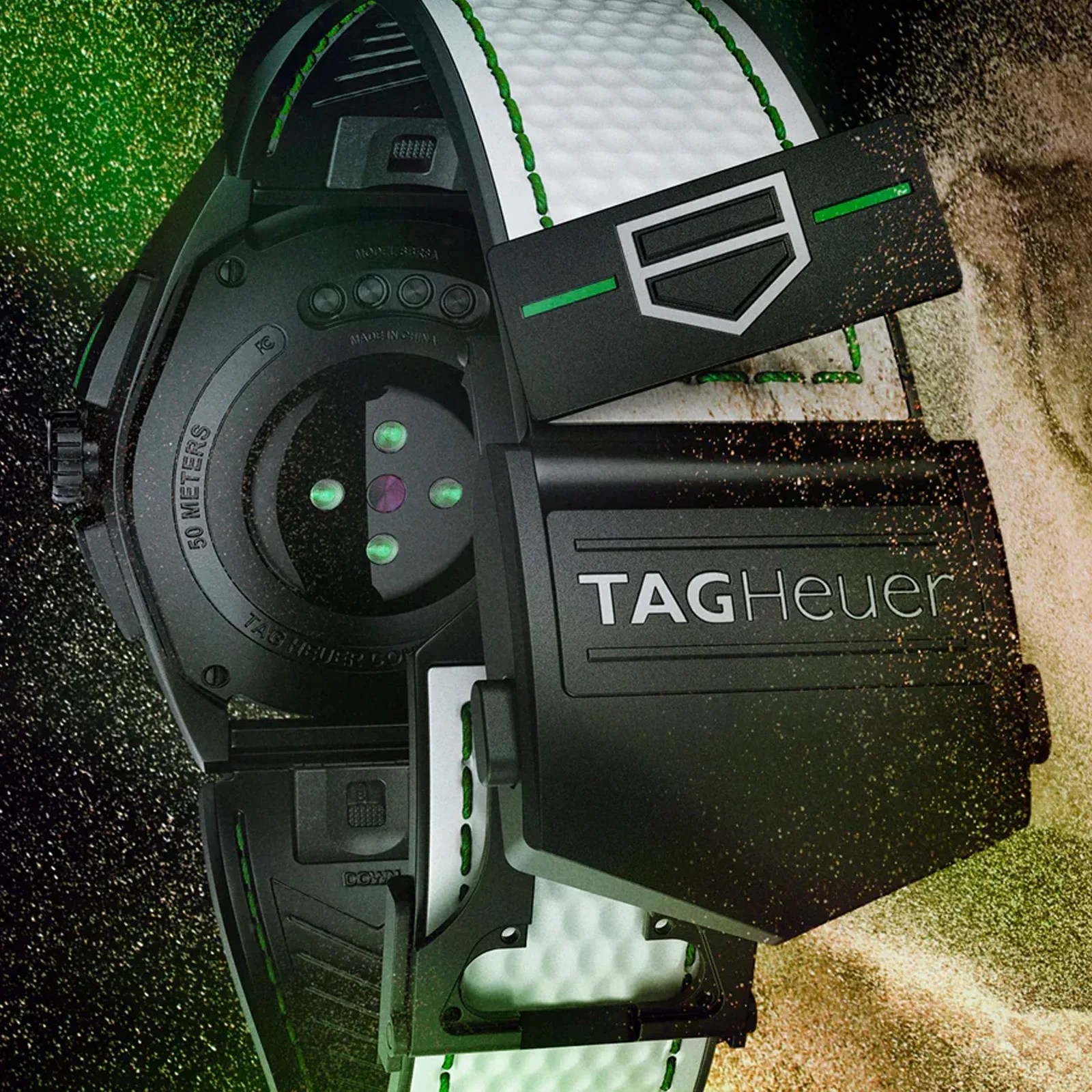 Close-up of the back of a TAG Heuer watch with a white textured strap featuring green stitching. The watch case is black with visible sensors and the TAG Heuer logo prominently displayed on a black clasp or cover. The watch is marked as water-resistant up to 50 meters.