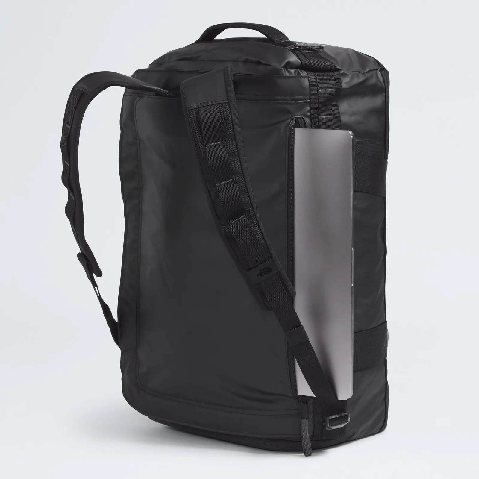 Black rectangular backpack with padded shoulder straps and a top handle, shown from the side with a laptop partially inserted into a vertical zippered compartment. The material appears smooth and slightly shiny.