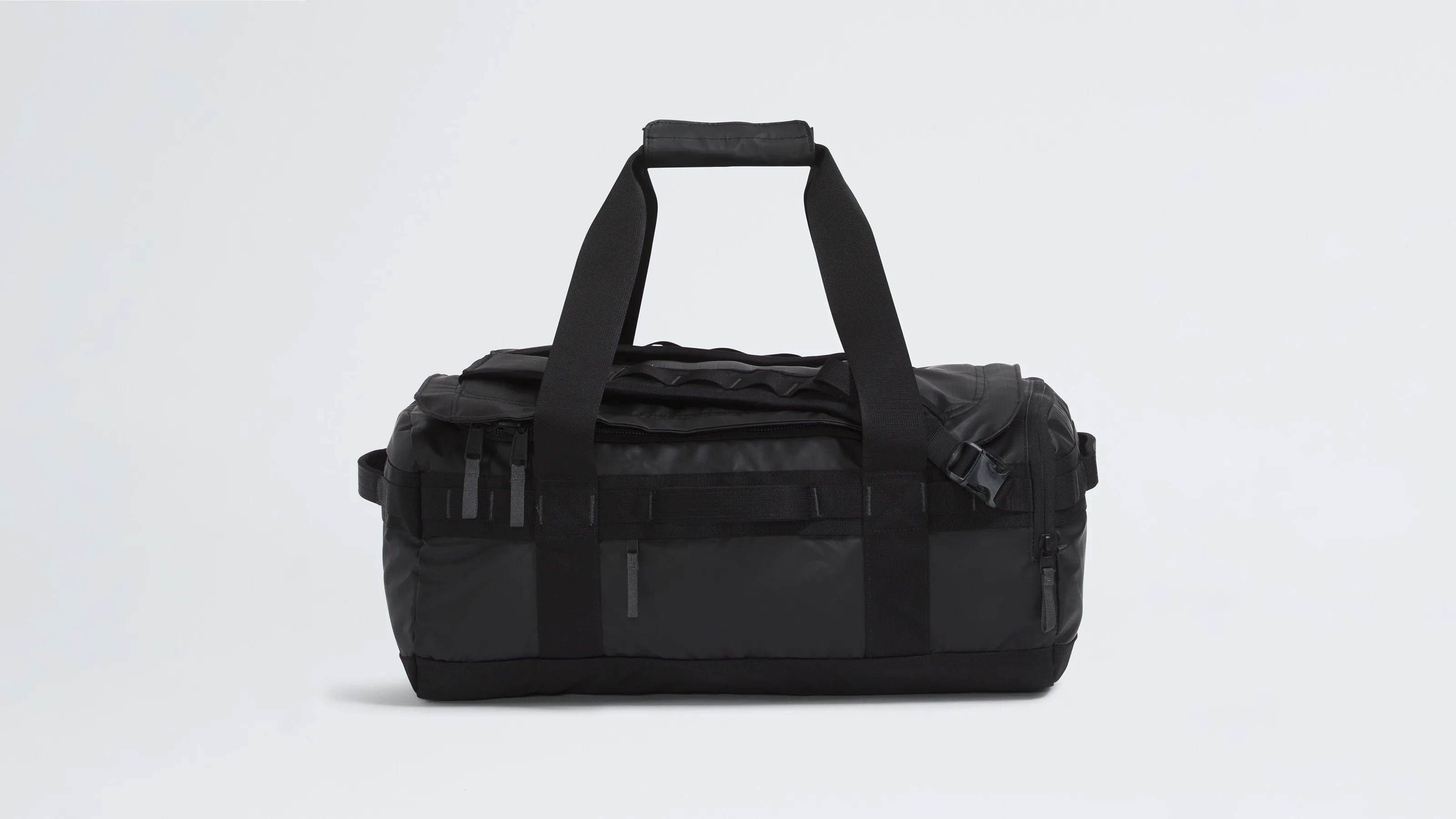 Black duffel bag with dual handles and a padded grip, featuring multiple zippered compartments and side straps, set against a plain light background.