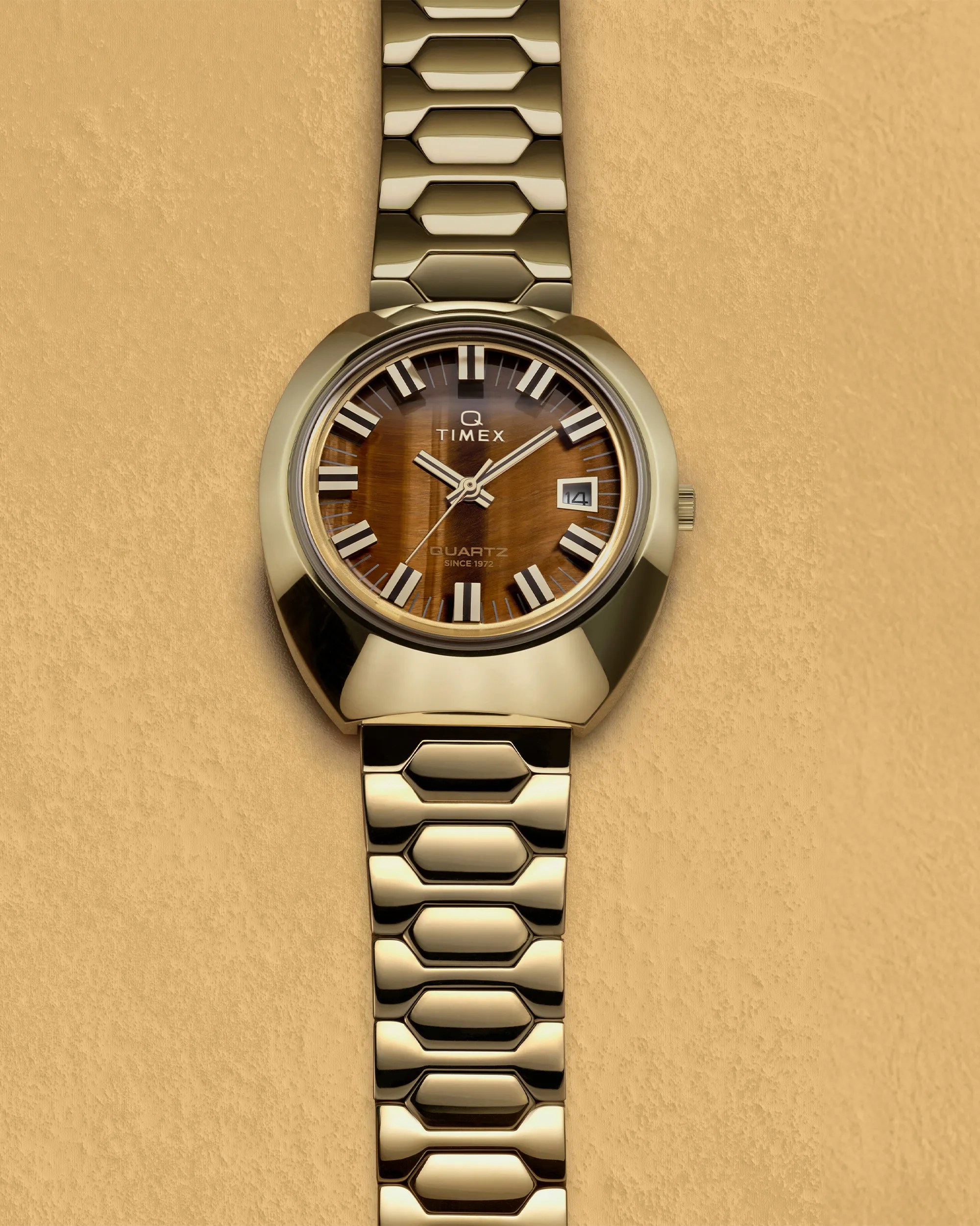 Gold-toned Timex wristwatch with a brown sunburst dial, featuring bold white hour markers and hands, a date window at 3 o'clock, and a distinctive hexagonal-link metal bracelet.