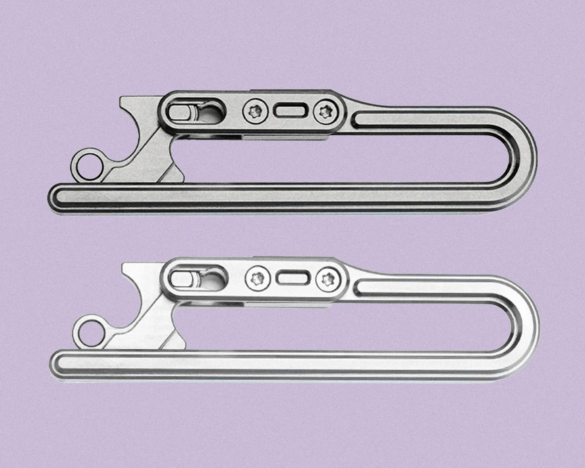 Two identical silver metal carabiner clips with a sleek, modern design are shown side by side on a light purple background. Each carabiner features a rounded rectangular loop and a locking mechanism with two screws and a sliding latch for secure closure. The top carabiner has a slightly darker outline compared to the bottom one.