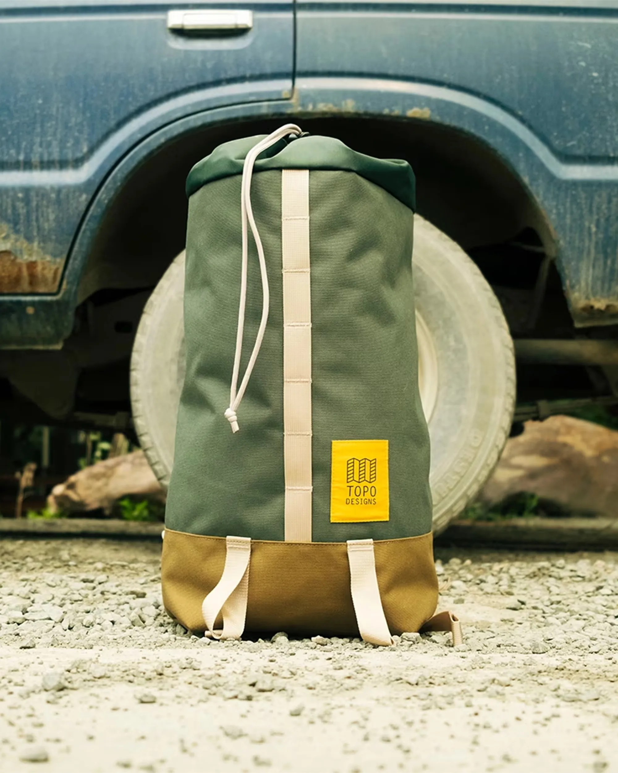Topo Designs Cosmos Backpack sitting in the dirt in front of a truck tire