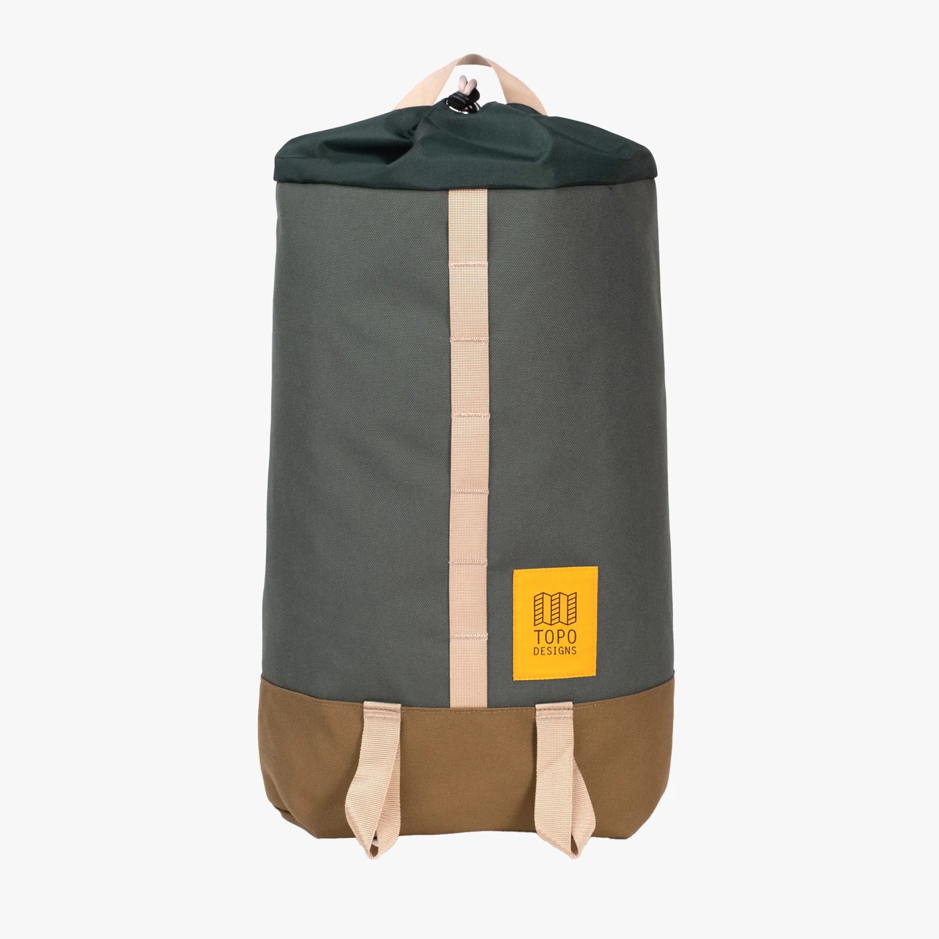 A cylindrical backpack with a dark green body, brown bottom, and beige vertical strap running down the center. It has a beige handle at the top and two beige loops at the bottom front. A yellow patch with the "TOPO DESIGNS" logo is sewn near the bottom right. The top closure appears to be a drawstring.