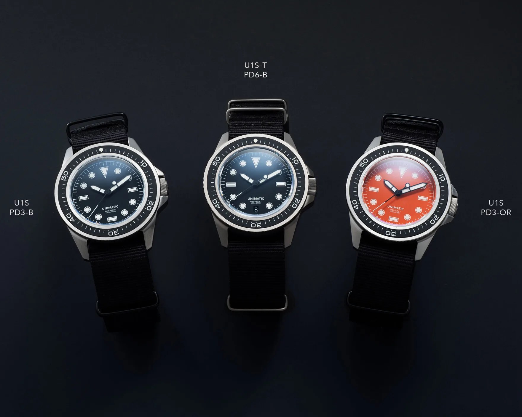 Three wristwatches with black straps are displayed on a dark surface. The left watch has a black dial labeled "U1S PD3-B," the middle watch has a dark blue dial labeled "U1S-T PD6-B," and the right watch has an orange dial labeled "U1S PD3-OR." Each watch features a rotating bezel with minute markers and luminous hour markers on the dial.