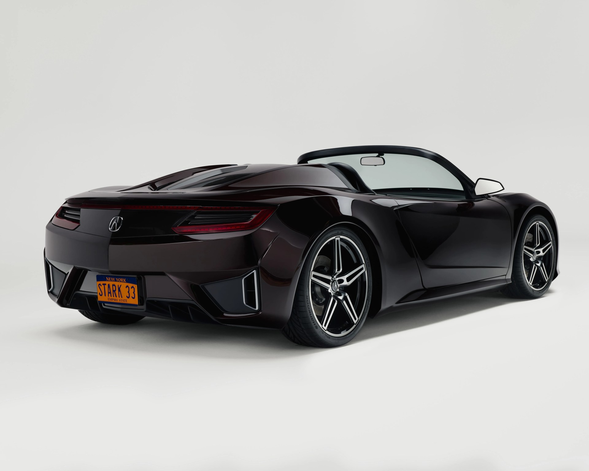 Sleek black convertible sports car with a low profile, featuring sharp, angular rear lights and a New York license plate reading "STARK 33." The car has large, stylish alloy wheels with a five-spoke design and a smooth, aerodynamic body.