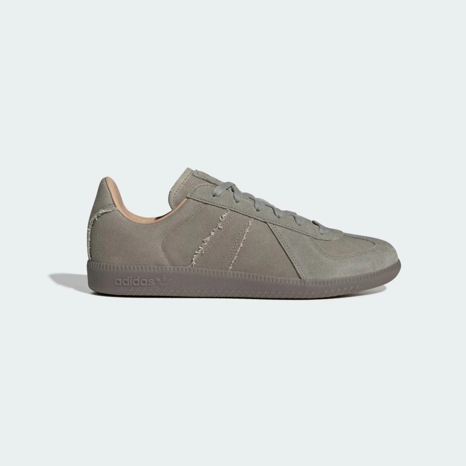 Low-top sneaker in muted gray with a textured fabric upper and suede overlays. Features gray laces, a rubber sole with the Adidas logo embossed near the heel, and subtle stitching details along the sides. The interior lining is a light beige color.