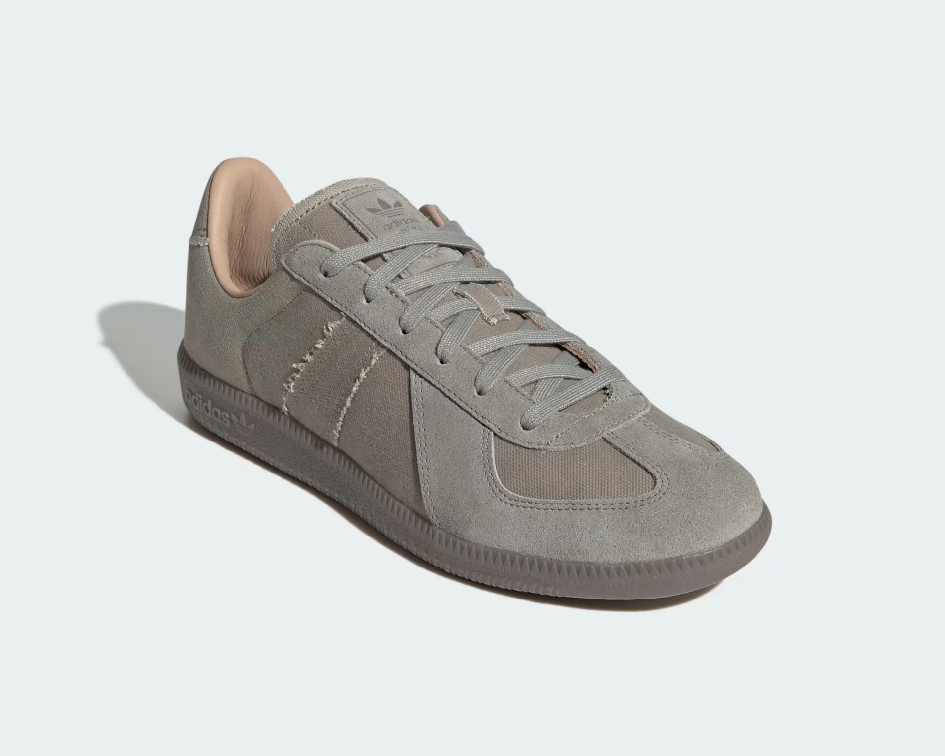 Gray suede and mesh Adidas sneaker with a low profile design, matching gray laces, and a textured rubber sole. The shoe features subtle Adidas branding on the tongue and side of the sole, with a light beige interior lining.