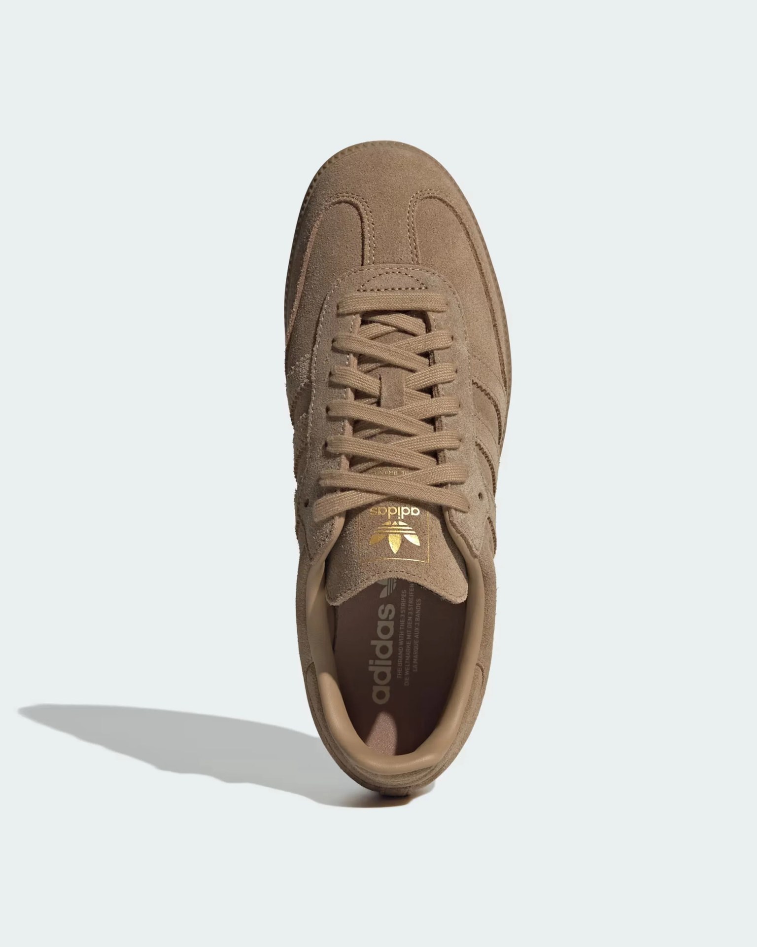 Light brown suede Adidas sneaker with matching laces, gold Adidas logo on the tongue, and a padded collar. The shoe has a classic design with visible stitching and a shadow cast to the left.