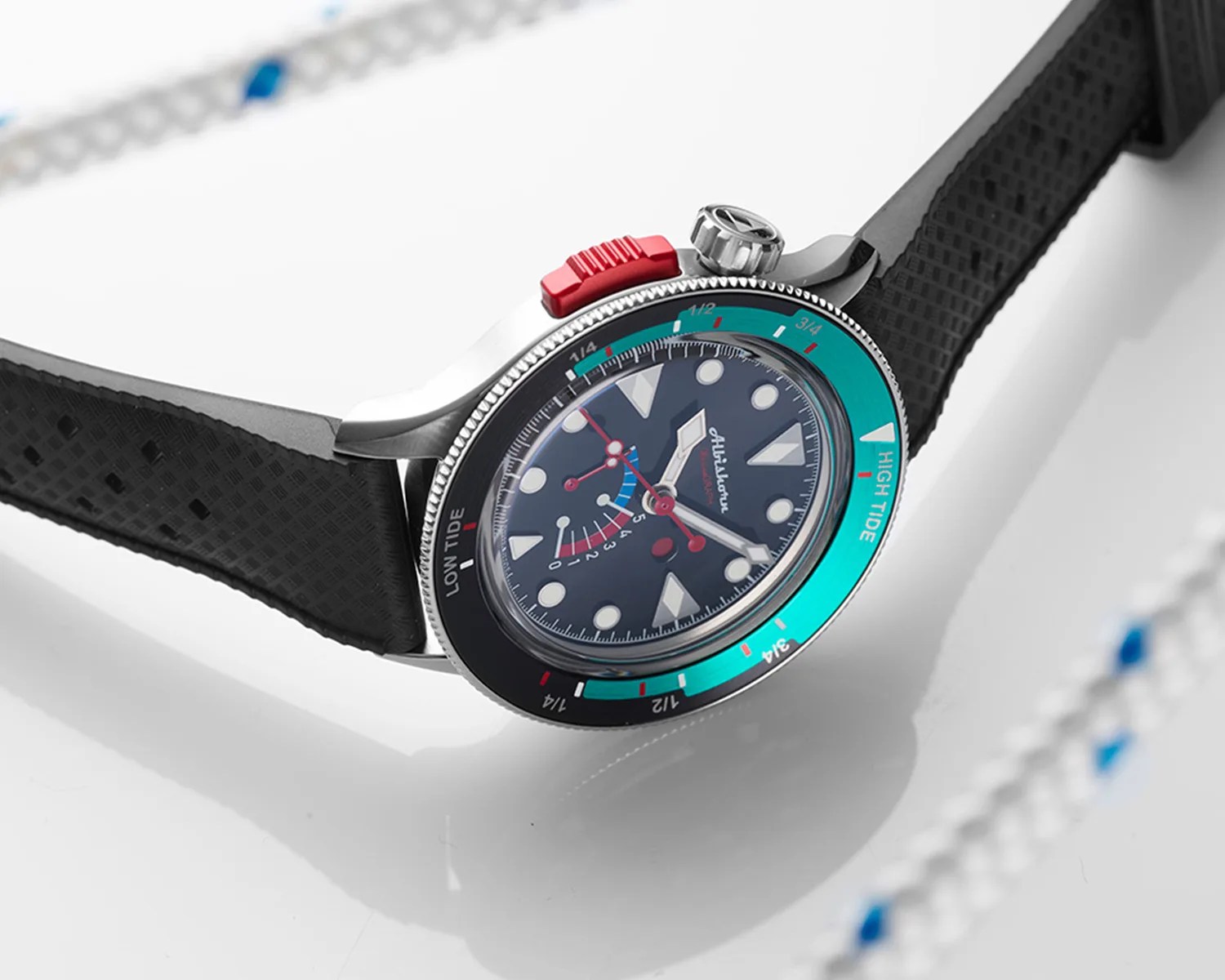 A wristwatch with a black textured rubber strap and a stainless steel case. The watch face is dark with large white circular and triangular hour markers. It has multiple red and white hands, including a second hand with a red tip. The bezel is divided into two colors: black on the left side labeled "LOW TIDE" and turquoise on the right side labeled "HIGH TIDE," with fractional markings in white and red. There is a prominent red button near the crown on the right side of the case. The brand name "Albishorn" is visible on the dial.