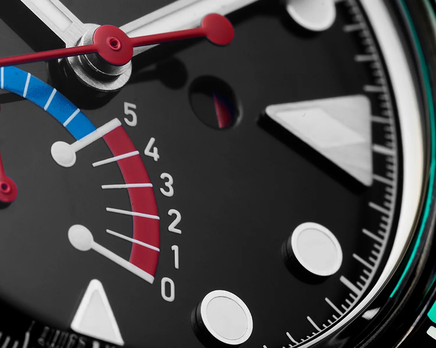 Close-up of a black watch dial featuring white triangular and circular hour markers, a red second hand, and a subdial with a blue and red segmented scale numbered from 0 to 5. The watch has detailed minute markers around the edge and a small circular window showing a red and blue indicator.