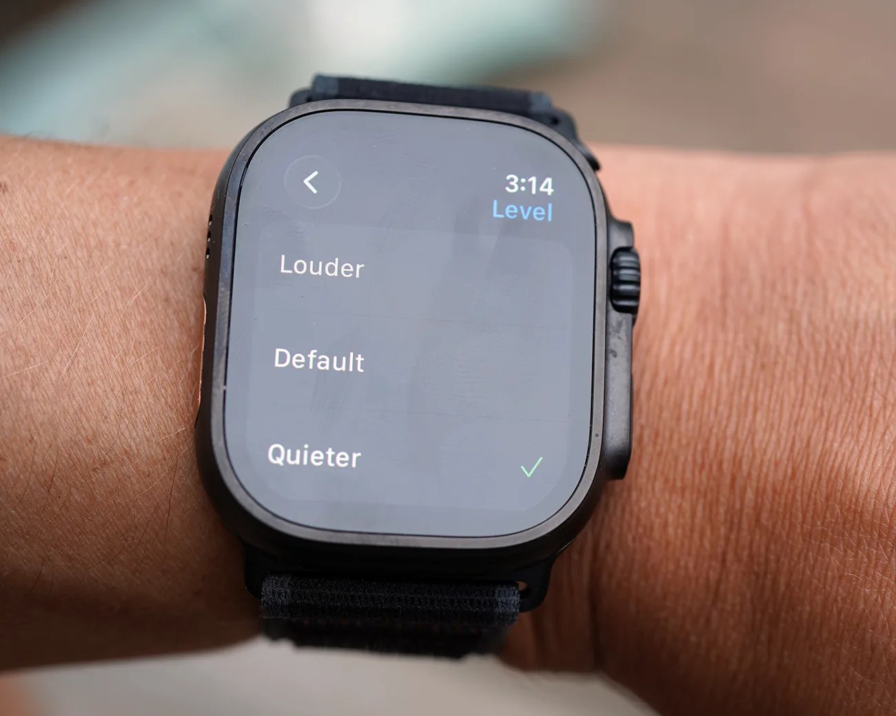 Smartwatch on a wrist displaying a settings menu with volume options: Louder, Default, and Quieter, with Quieter selected. The time shown is 3:14.