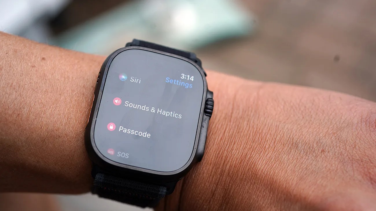 A black smartwatch on a wrist displaying the settings menu with options for Siri, Sounds & Haptics, Passcode, and SOS. The time shown is 3:14.