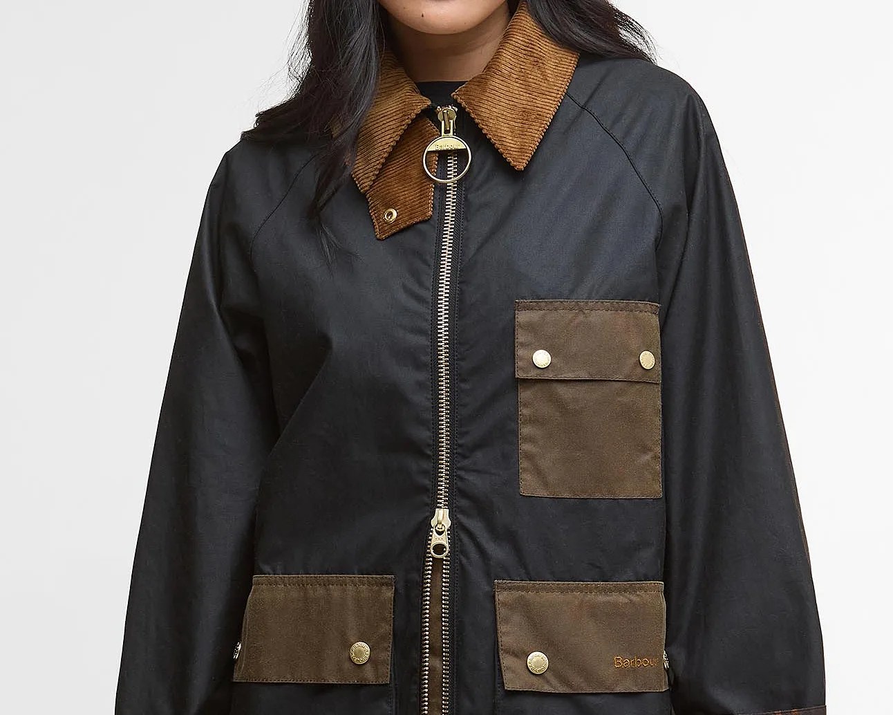 Black jacket with a brown corduroy collar, featuring a front zipper with a large round pull. The jacket has two brown flap pockets with snap buttons on the lower front and one brown flap pocket with snap buttons on the upper left chest. The lower right pocket has the brand name "Barbour" embroidered in brown.