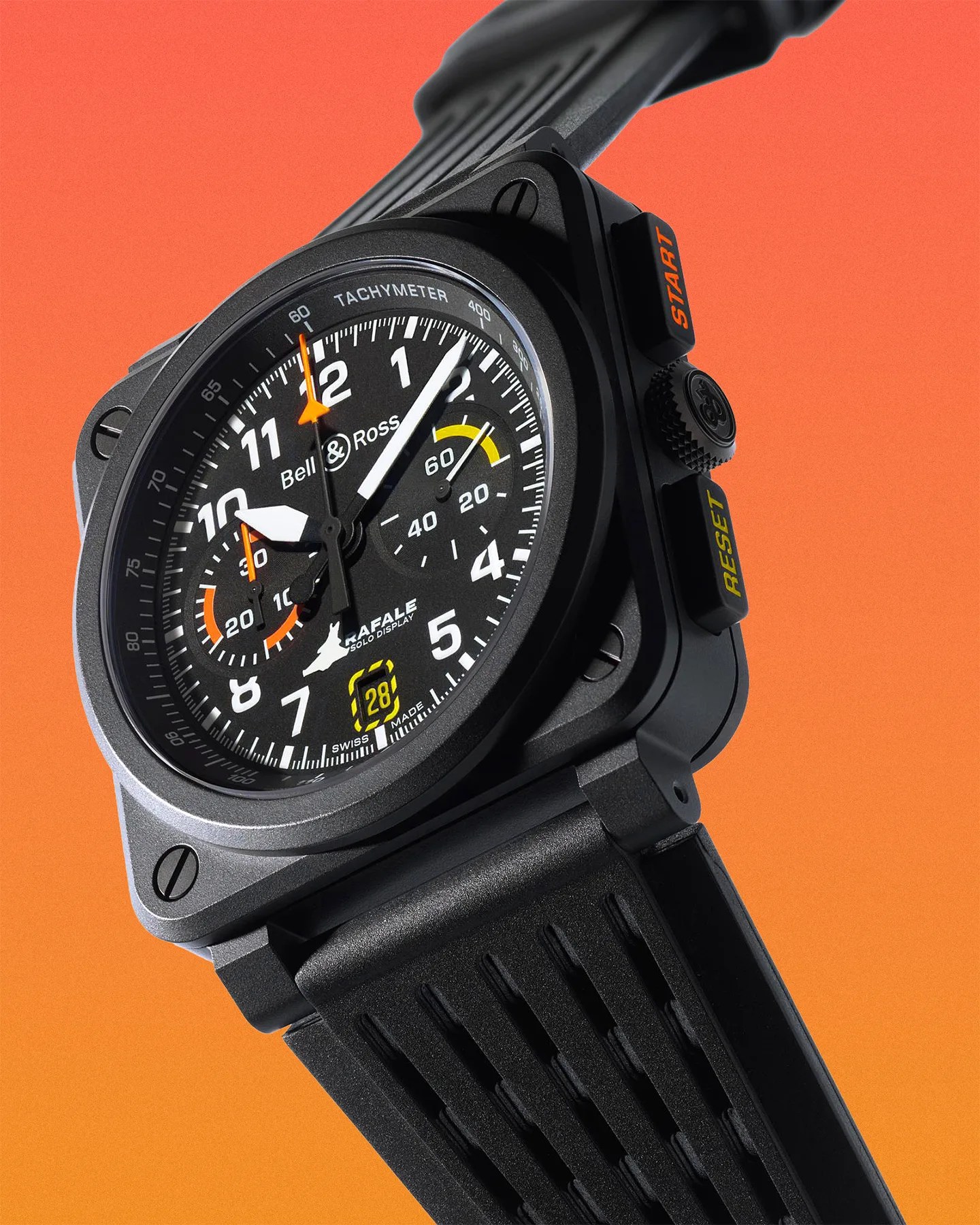 Black Bell & Ross wristwatch with a square case and round dial featuring white numerals and hands, orange and yellow accents, and a tachymeter scale. The dial includes subdials, a date display at 6 o'clock, and the text "RAFALE SOLO DISPLAY" with a small jet graphic. The watch has two black buttons on the side labeled "START" and "RESET" in orange and yellow, and a textured black rubber strap. The background is a gradient of orange shades.