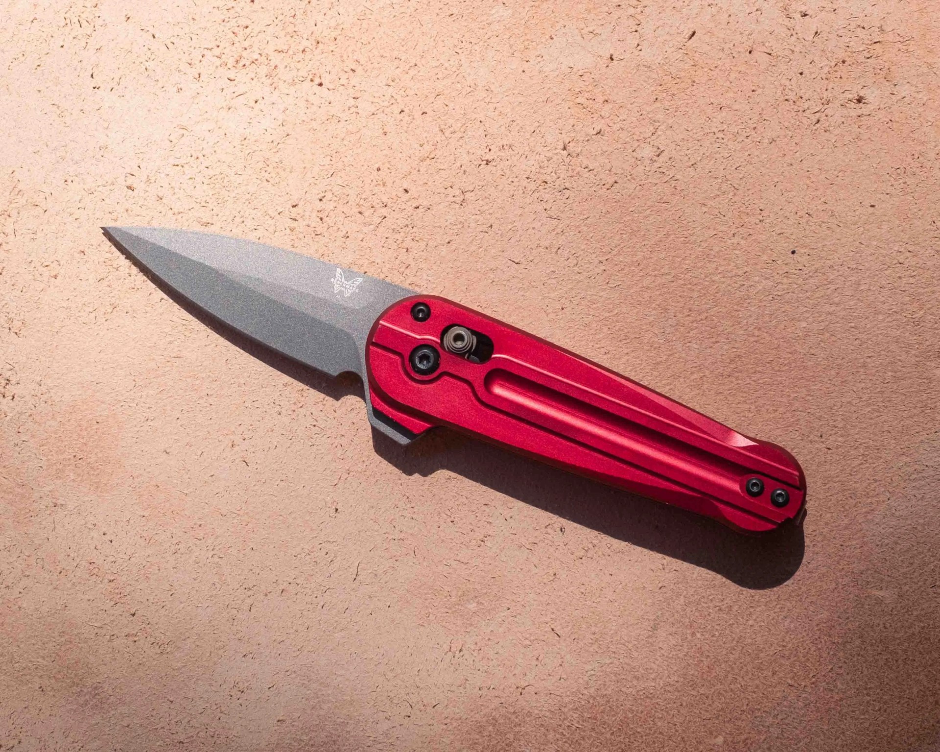 Folding knife with a stonewashed steel blade and a red anodized aluminum handle, featuring a butterfly logo on the blade near the handle.