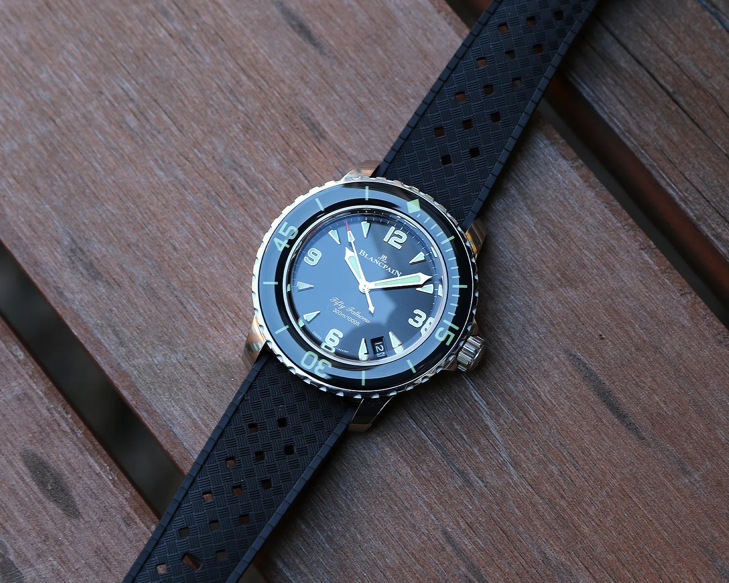Black Blancpain Fifty Fathoms dive watch with a stainless steel case, luminous markers, and a black textured rubber strap, placed on a wooden surface.