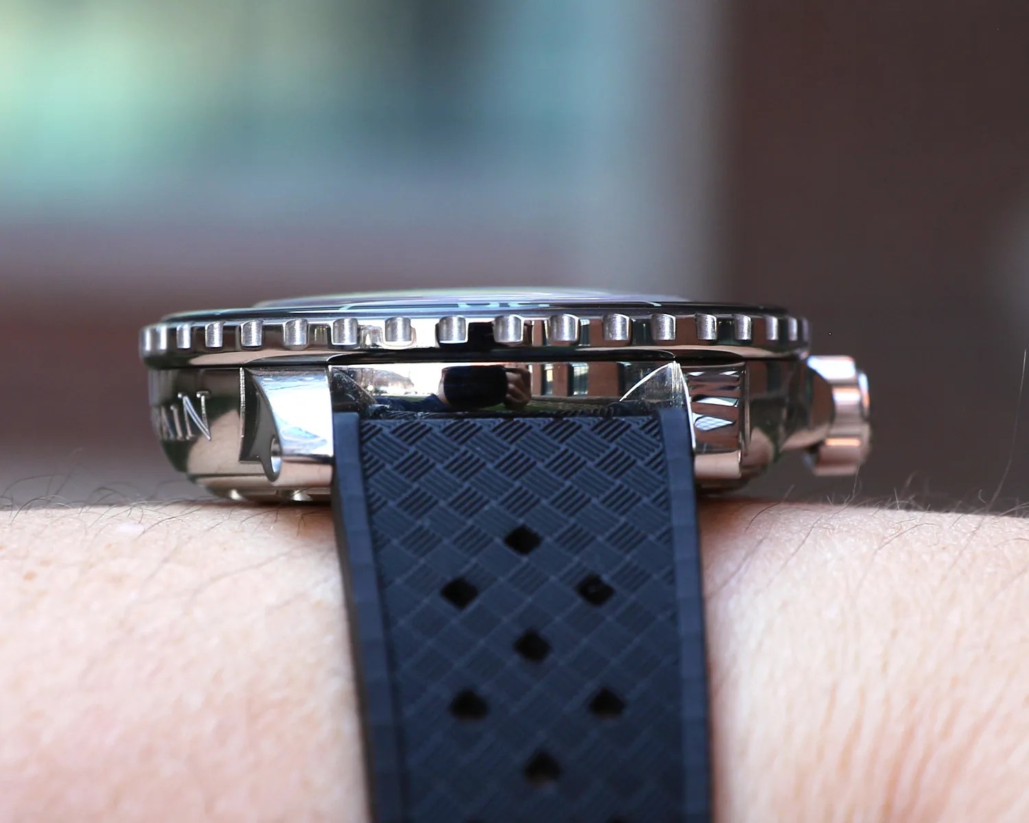 Close-up side view of a blancpain wristwatch with a polished metal case and a textured black rubber strap, worn on a person's wrist. The watch bezel has a ridged edge, and the crown is visible on the right side. The watch case reflects the surroundings.