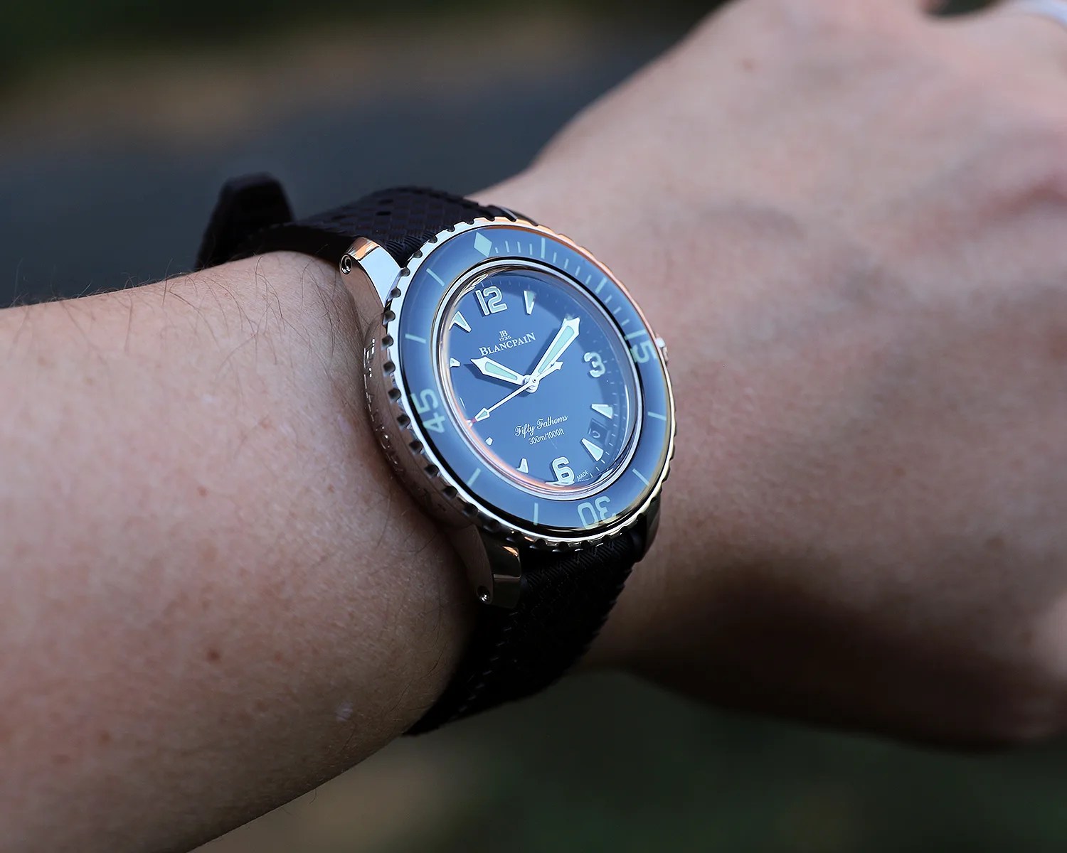 Blancpain Fifty Fathoms wristwatch with a black dial, luminous hands and markers, a rotating bezel, and a black textured strap, worn on a person's wrist.