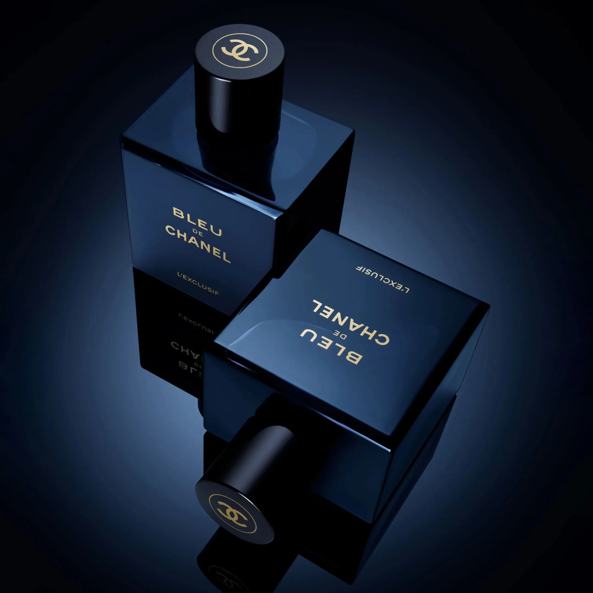 Two dark blue square bottles of Bleu de Chanel L'Exclusif perfume with black caps featuring the Chanel logo in gold, placed on a reflective surface with a gradient blue background.