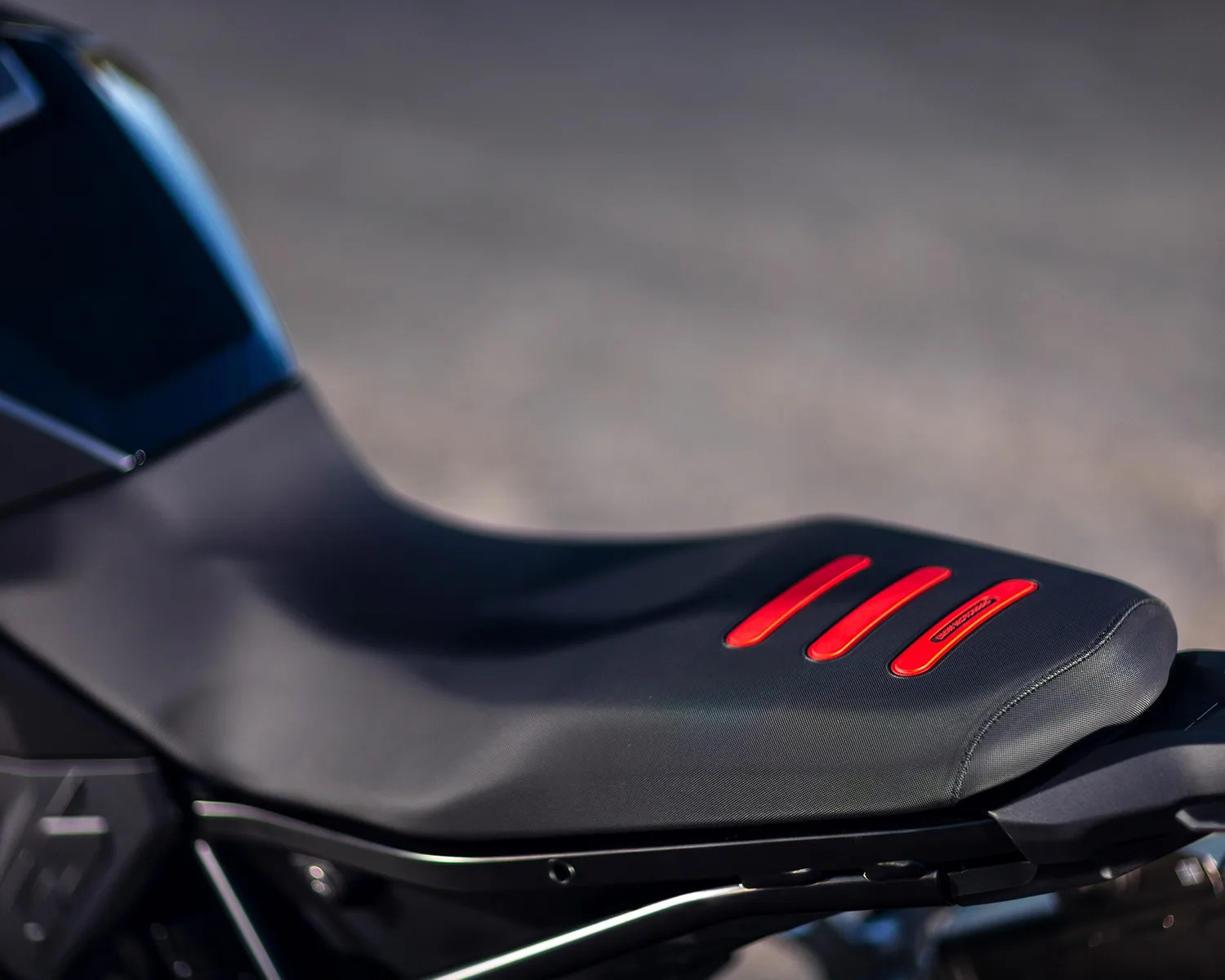Close-up of a black motorcycle seat with three red accents on the rear section, featuring a sleek and smooth design.