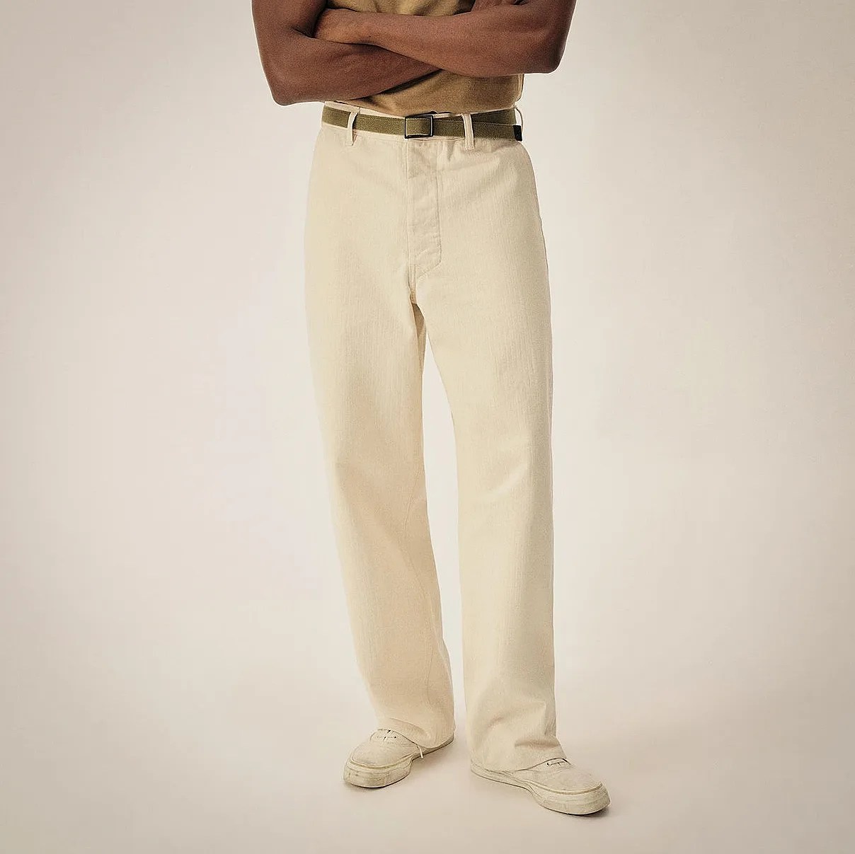 Straight-leg cream-colored pants paired with a matching cream belt and off-white sneakers. The pants have a clean, minimal design with a subtle texture.