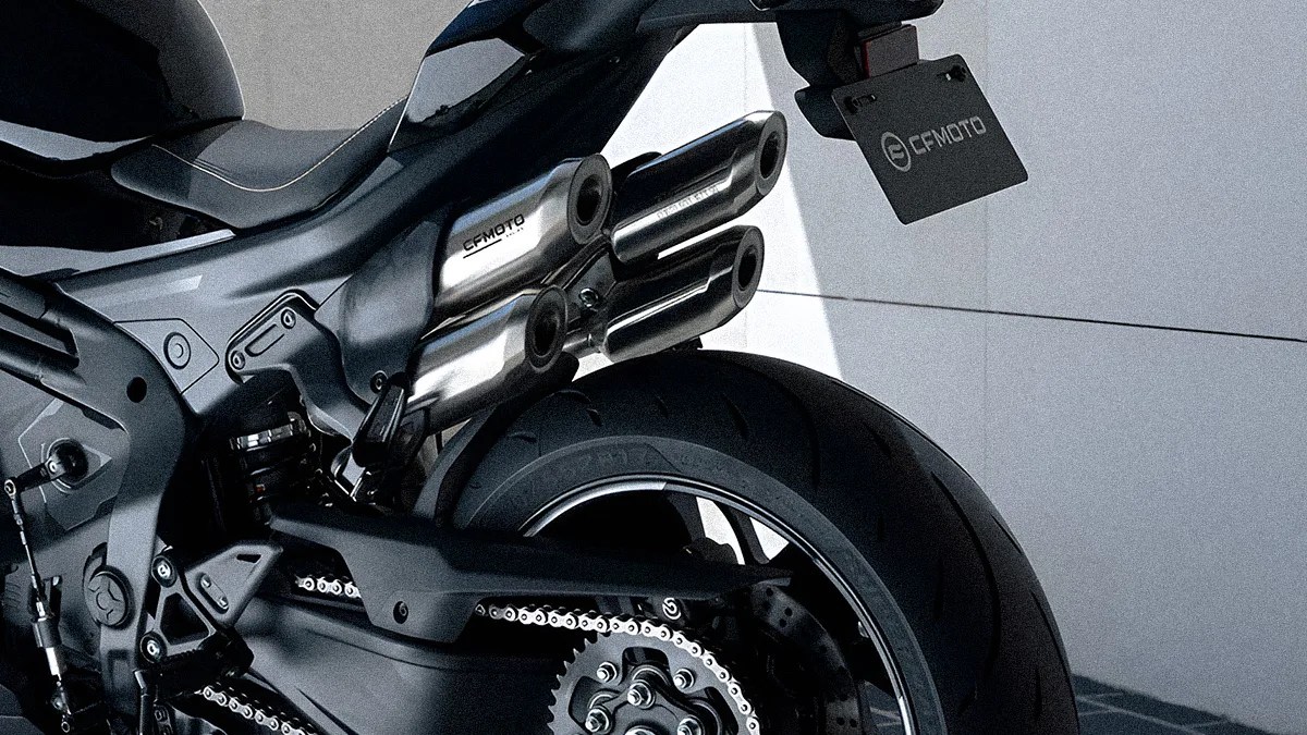 Rear section of a black motorcycle showing the rear tire, chain, and triple exhaust pipes with "CFMOTO" branding on the exhaust and license plate. The motorcycle has a sleek, modern design with a visible suspension spring and detailed mechanical components.