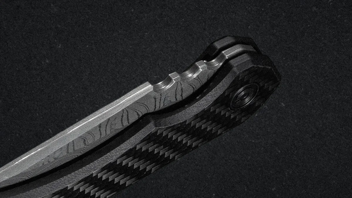 Close-up of a folding knife handle and partially visible blade. The blade has a patterned texture, likely Damascus steel, and the handle features a carbon fiber design with a textured grip and a pivot screw. The background is dark and textured.