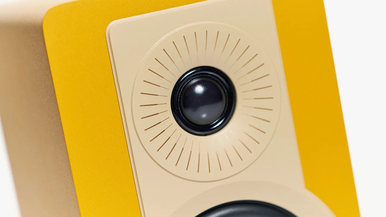 Close-up of a yellow and beige speaker with a black tweeter surrounded by radial lines.