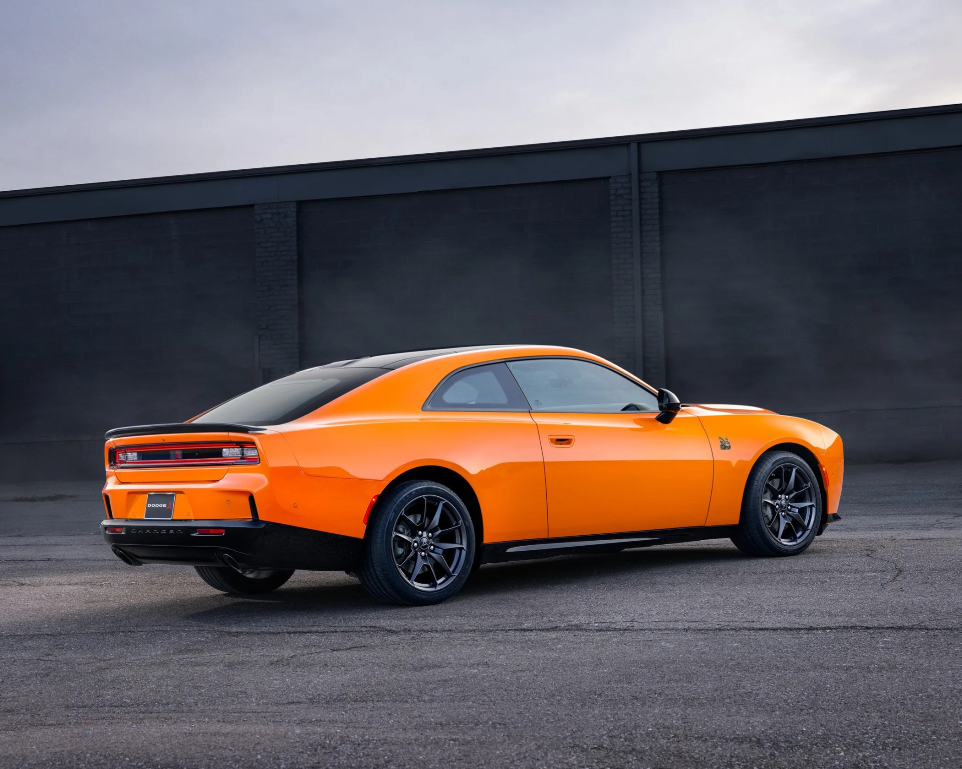 a photo of an orange dodge muscle car parked in front of a grey wall