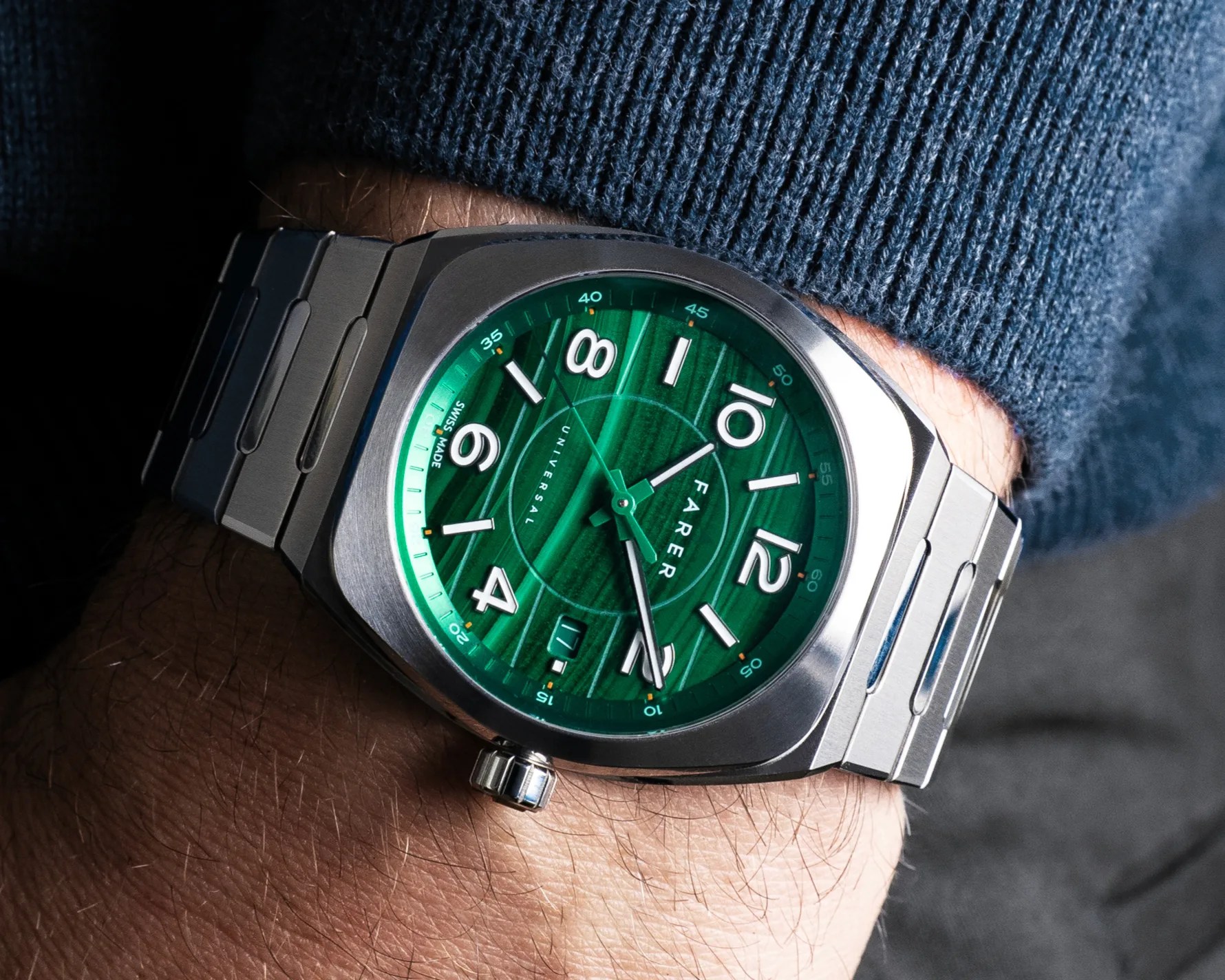 Stainless steel wristwatch with a green textured dial featuring white Arabic numerals and minute markers. The watch has a date window at the 6 o'clock position and the brand name "FARER" displayed on the dial. The watch is worn on a wrist with a blue knitted sleeve visible.
