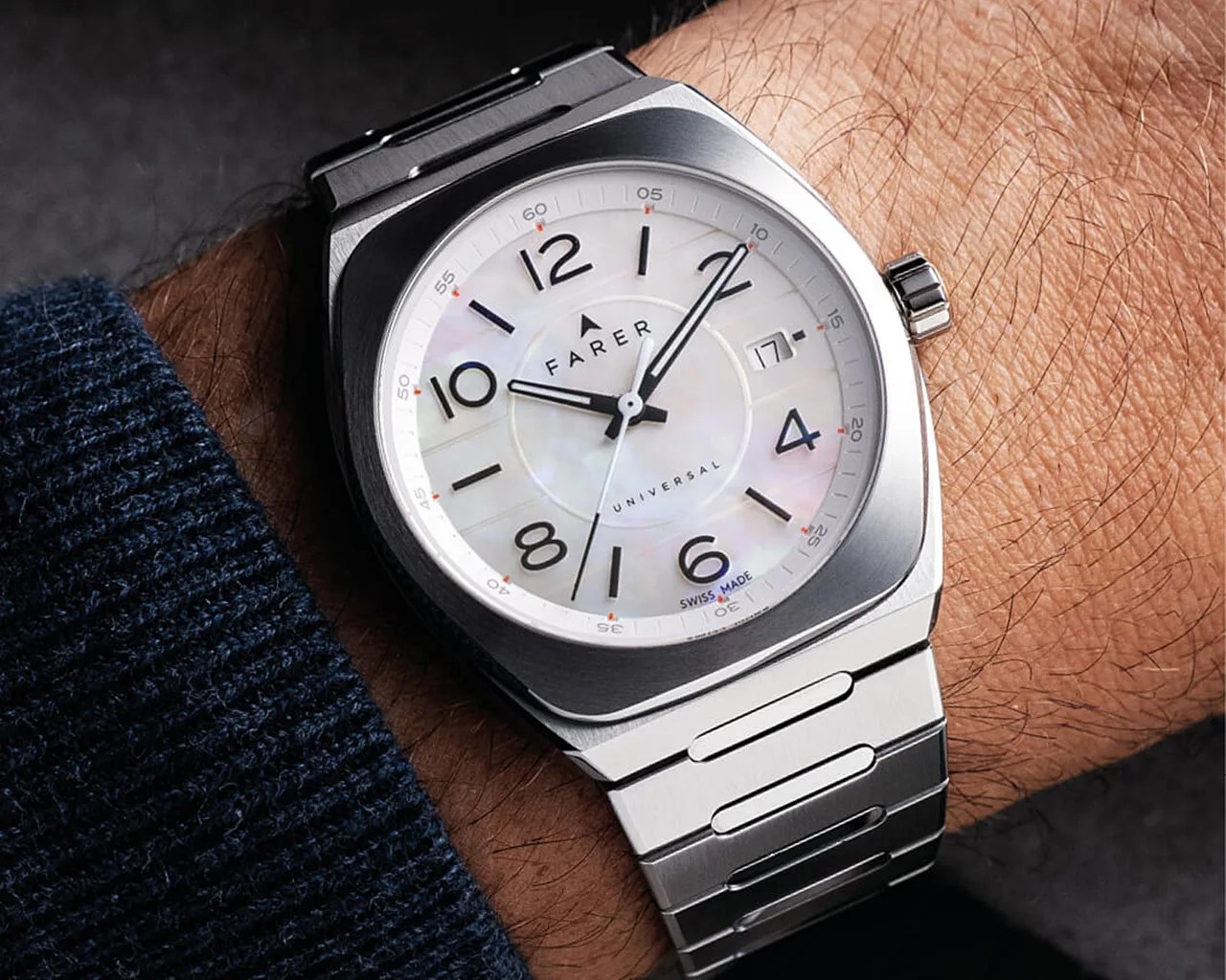 Silver wristwatch with a white mother-of-pearl dial, black Arabic numerals, and black hands. The watch features a date window at the 3 o'clock position and a second hand. The brand name "FARER" and the word "UNIVERSAL" are printed on the dial, along with "SWISS MADE" near the 6 o'clock position. The watch has a brushed metal case and a matching metal bracelet.