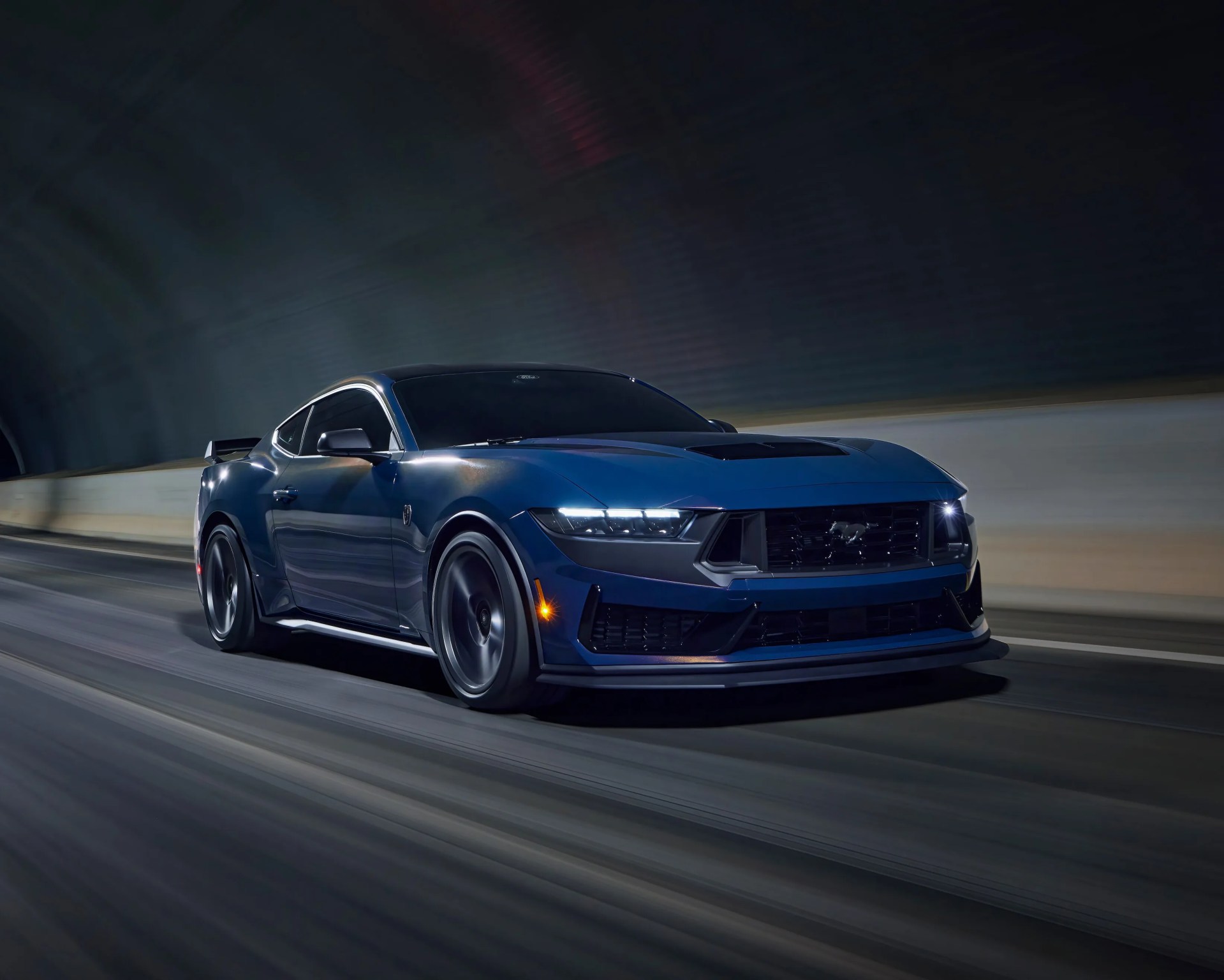 Blue Ford Mustang sports car driving through a tunnel at night, with headlights on and motion blur on the road.