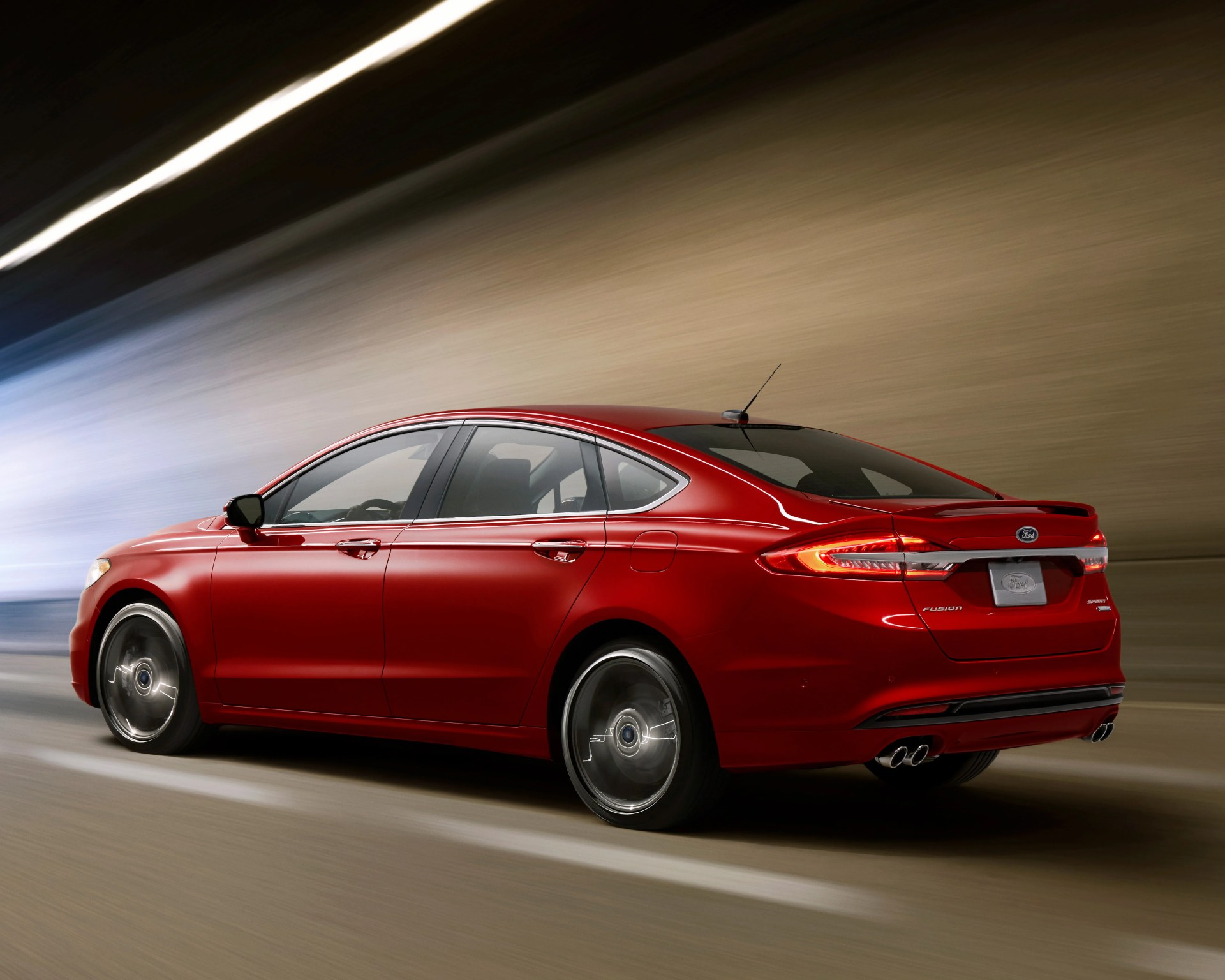 Red Ford Fusion sedan driving in a tunnel, shown from the rear side with motion blur on the wheels and background. The car features a rear spoiler, dual exhaust pipes, and illuminated taillights.