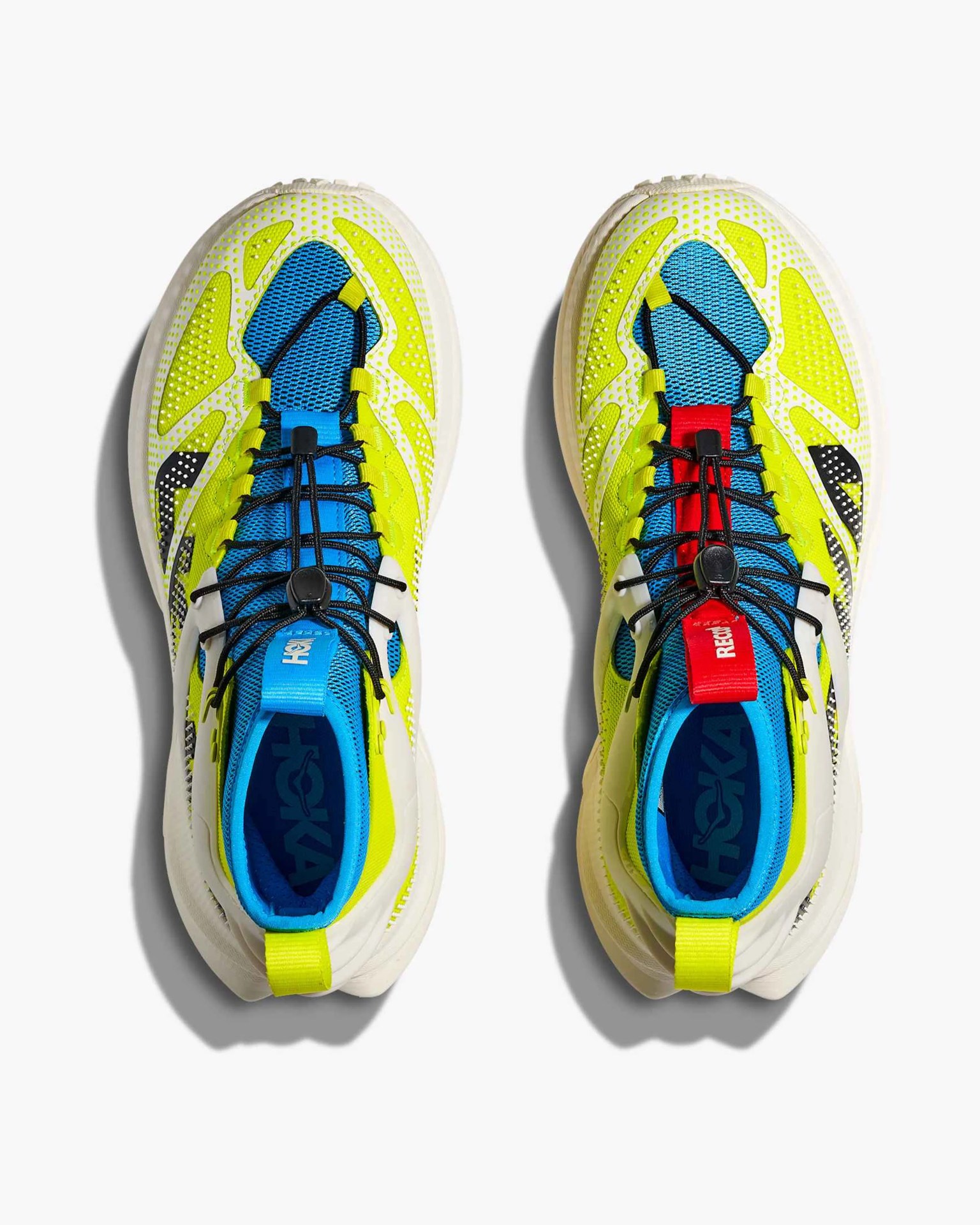 Pair of athletic shoes with a vibrant design featuring bright yellow, blue, and white colors. The shoes have a mesh upper with yellow overlays and black accents. The left shoe has a blue pull tab, while the right shoe has a red pull tab. Both shoes have black elastic laces with a toggle for adjustment. The interior lining is blue, and the soles are white with a textured pattern.