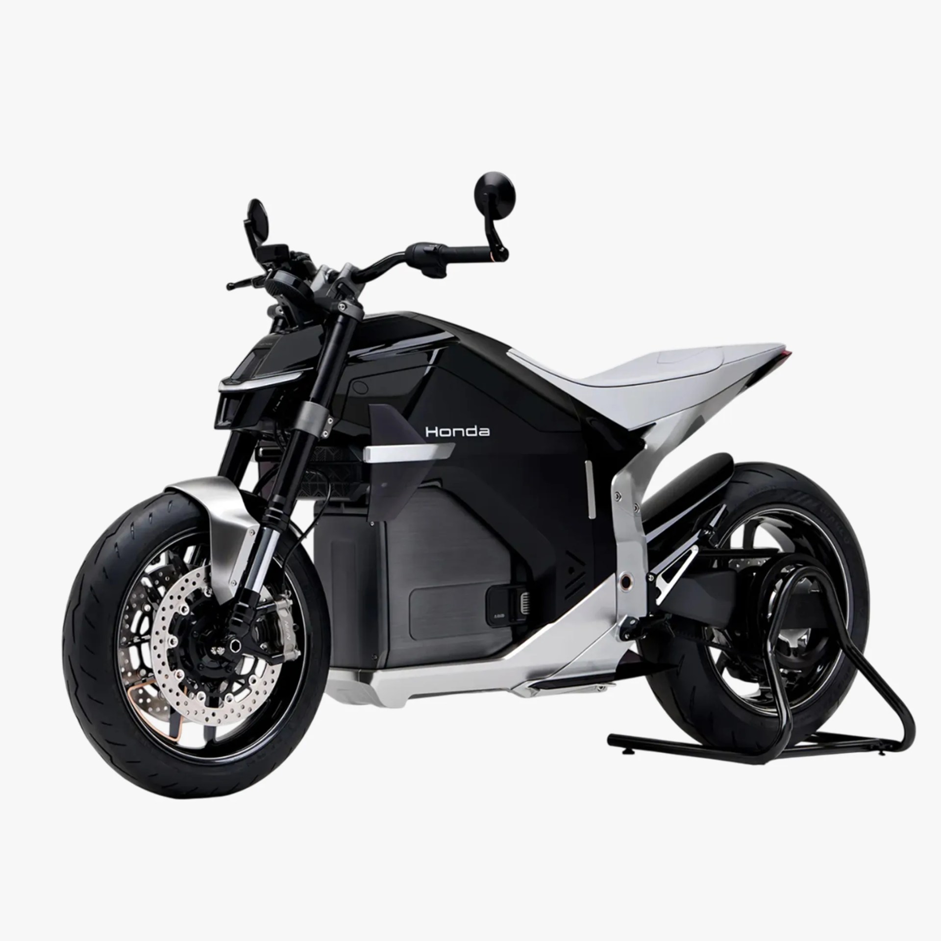 A sleek, modern Honda electric motorcycle with a black and silver body. It features a minimalist design with a solid frame, large front and rear tires, disc brakes, and a white seat. The bike is supported by a rear stand.