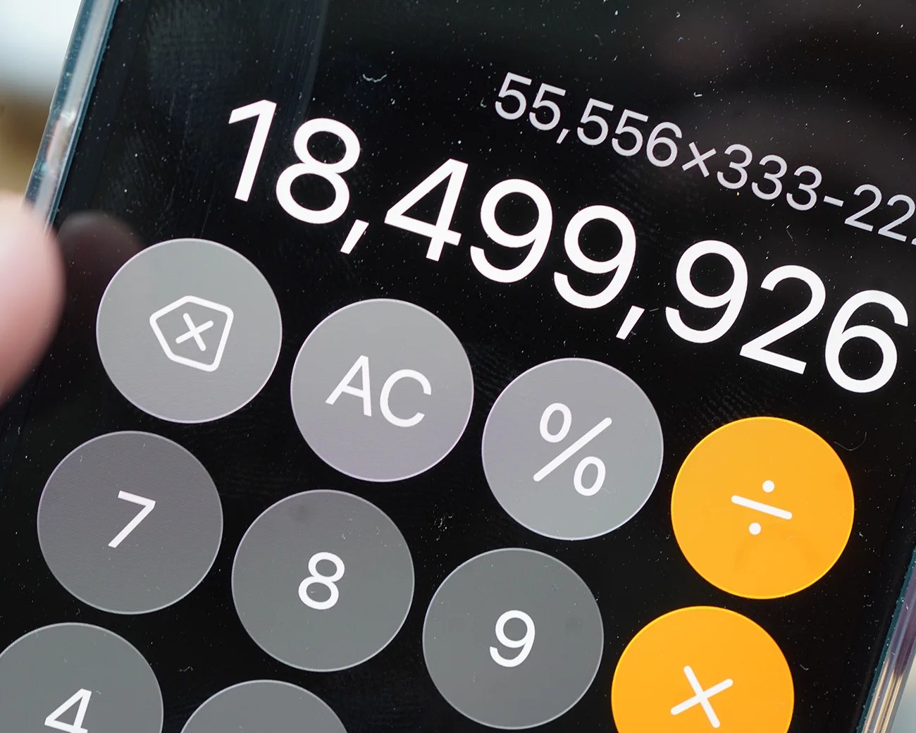 A smartphone calculator app displaying the result 18,499,926 from the calculation 55,556 × 333 - 22. The calculator buttons visible include clear (AC), percentage (%), division (÷), multiplication (×), and numbers 7, 8, and 9. The division and multiplication buttons are highlighted in orange.