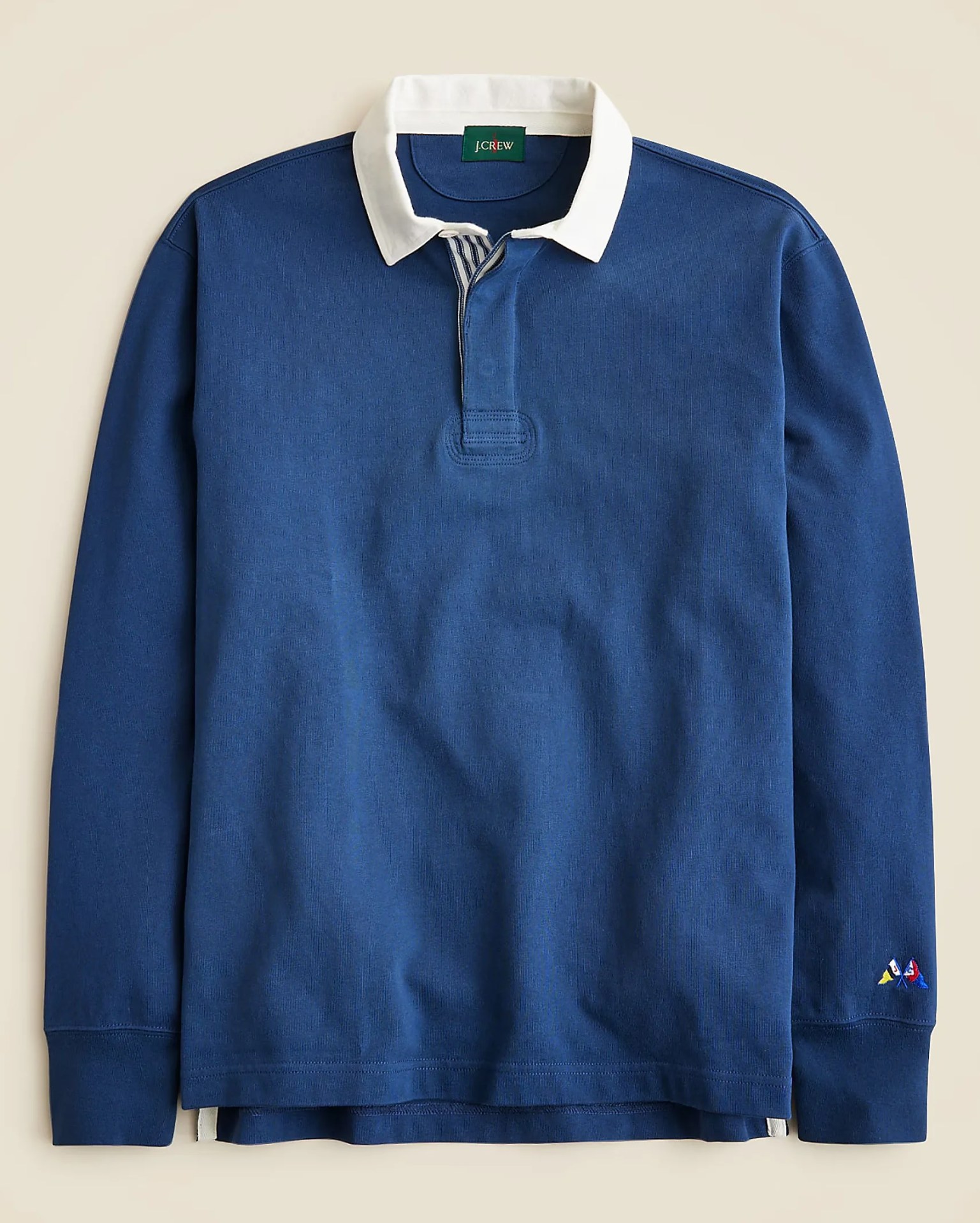 Long-sleeve navy blue rugby shirt with a white collar, a partial button placket, and small embroidered nautical flags on the left cuff.
