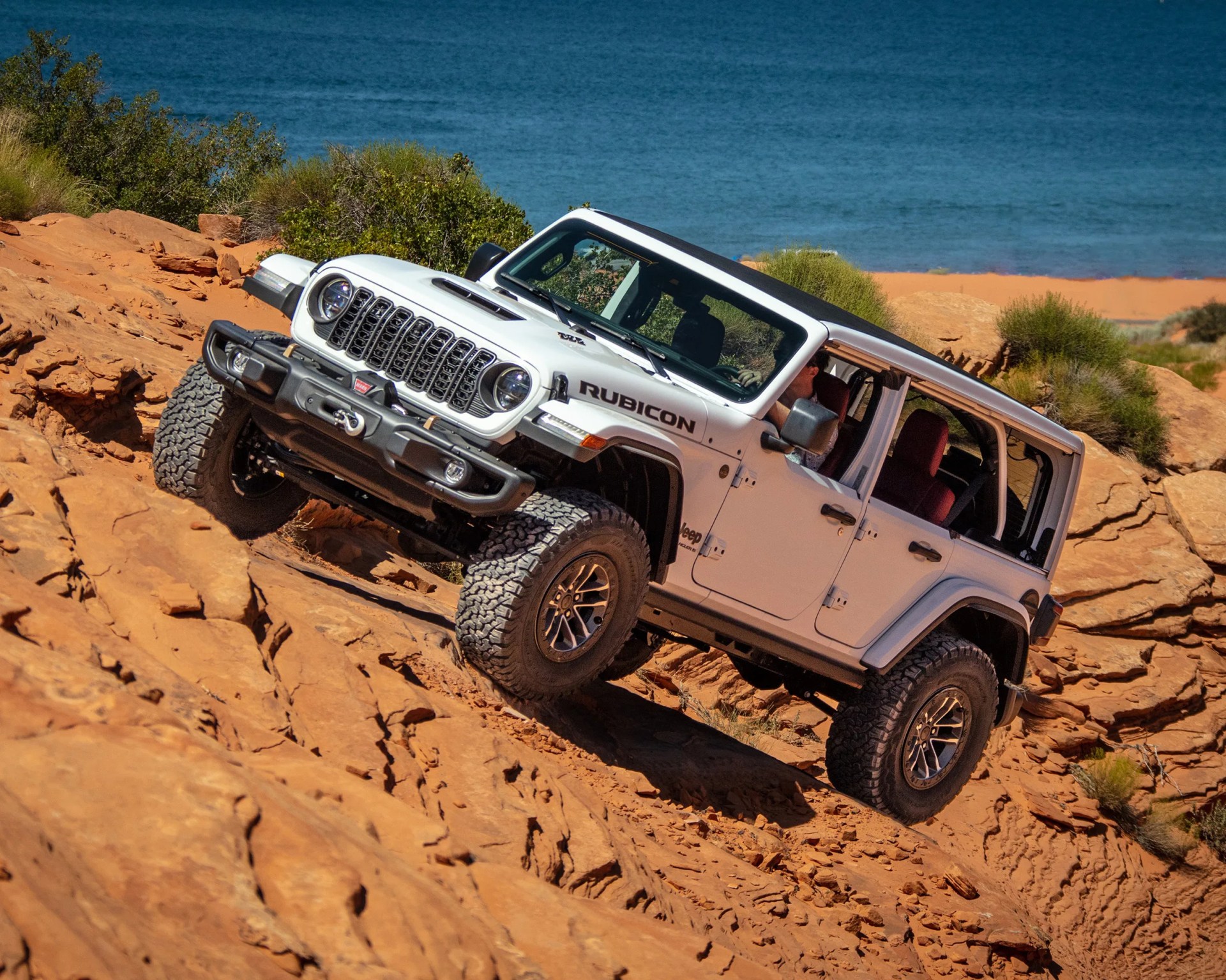 a white jeep wrangler four-door on a slope in front of the ocean