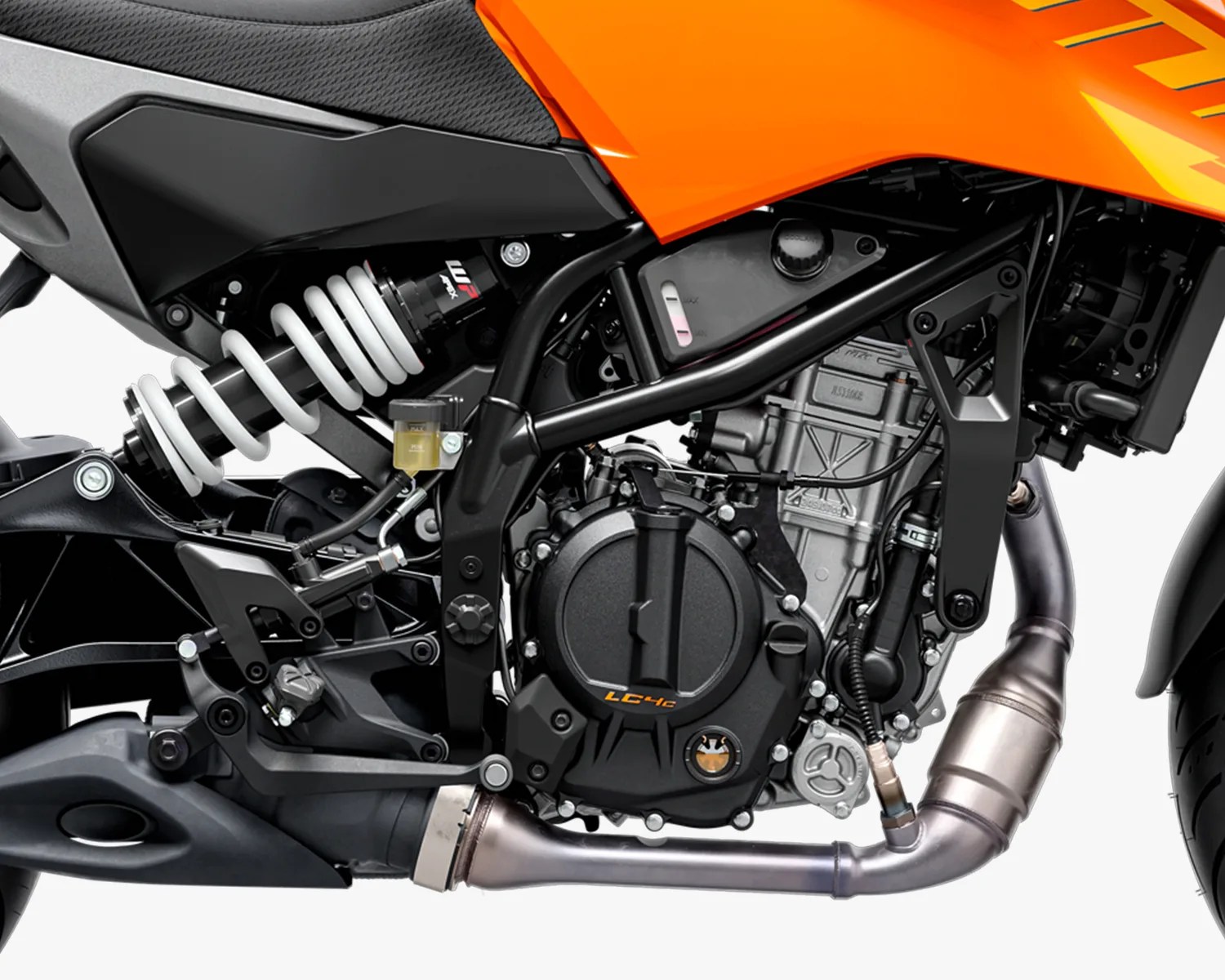 Close-up of a motorcycle engine and rear suspension system, featuring a black engine casing labeled "LC4c," a silver exhaust pipe, a white coil spring shock absorber, and part of the orange bodywork above. The frame and various mechanical components are visible, with a small fluid reservoir attached near the suspension.