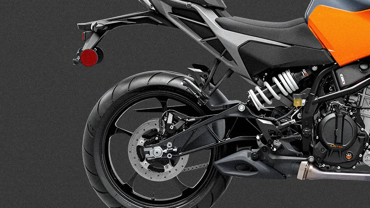 Rear section of a motorcycle featuring a large black rear tire with a disc brake, a black swingarm, a white coil spring suspension, and part of an orange and black body panel. The background is dark gray.