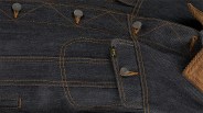 Dark denim fabric with orange stitching, featuring metal buttons and a small tag with the brand name "Lee" in yellow. The fabric also includes a section of brown corduroy material.