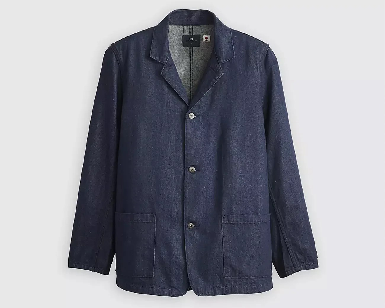 Dark blue denim jacket with a notched collar, three front buttons, and two large patch pockets at the lower front. The jacket has long sleeves and visible stitching details.