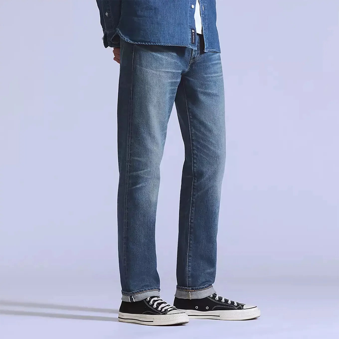 Straight-leg blue jeans with a slightly faded wash, rolled up at the cuffs, worn with black and white low-top sneakers.