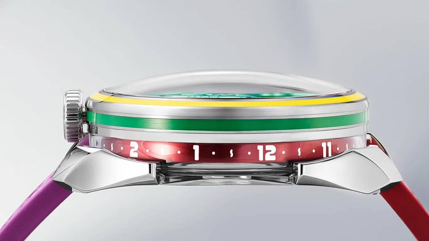 Side view of a M.A.D.Editions wristwatch with a domed crystal, a silver case, and a colorful bezel featuring yellow and green stripes. The watch has a red ring with white numerals and dots around the edge, and the strap is two-toned with purple on the left and red on the right. The crown is silver and textured for grip.
