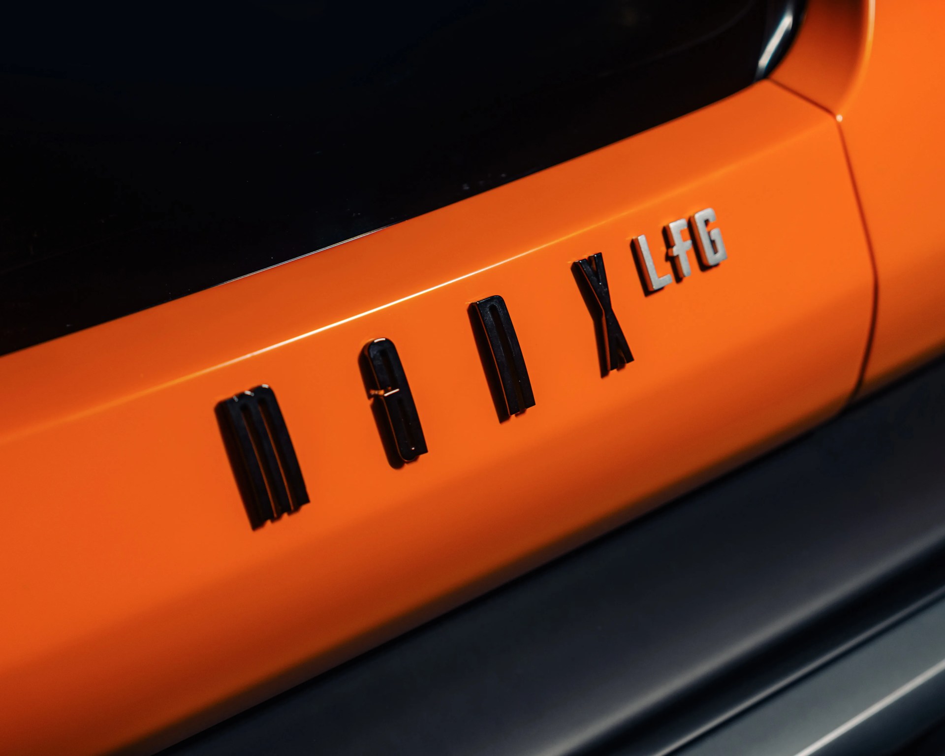 Orange car door panel with black and silver letters spelling "MEI X LfG" near the window and black trim below.