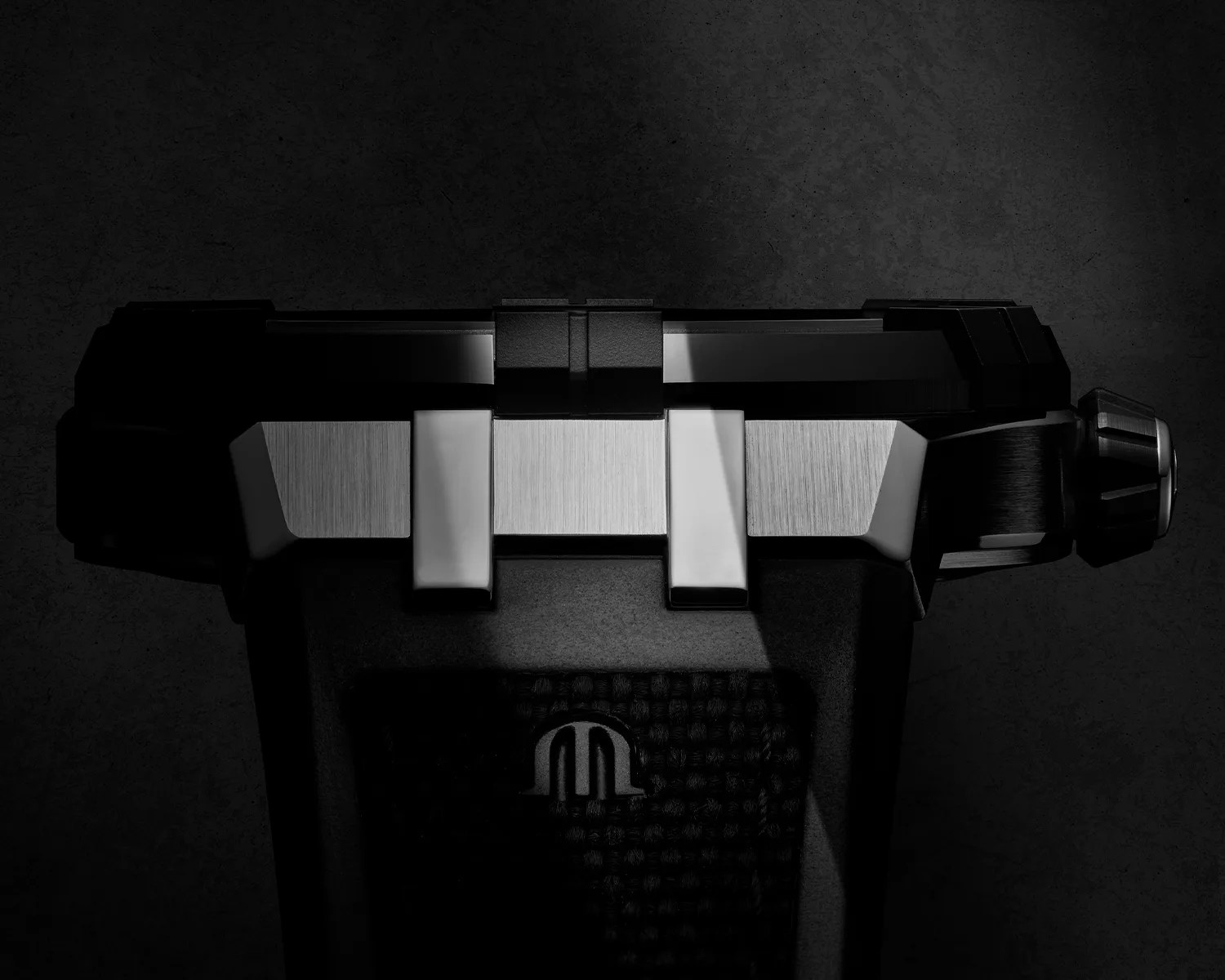 Close-up of a maurice lacroix watch crown and case side, featuring brushed metal and ceramic surfaces and a textured black strap with a subtle logo. The lighting highlights the metallic details against a dark background.