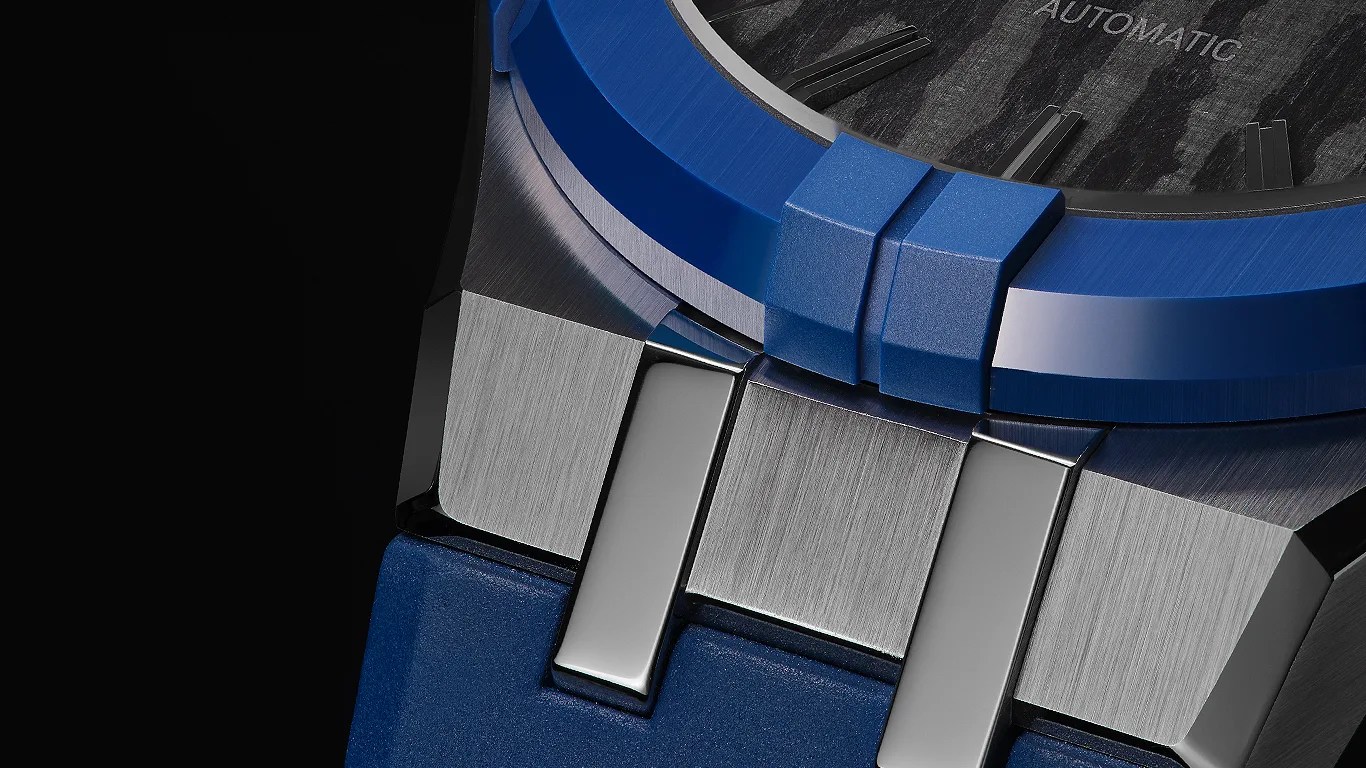 Close-up of a maurice lacroix watch featuring a blue bezel and strap, with a brushed metal case and polished metal links connecting the strap to the case. The watch dial is partially visible, showing a textured pattern and the word "AUTOMATIC.